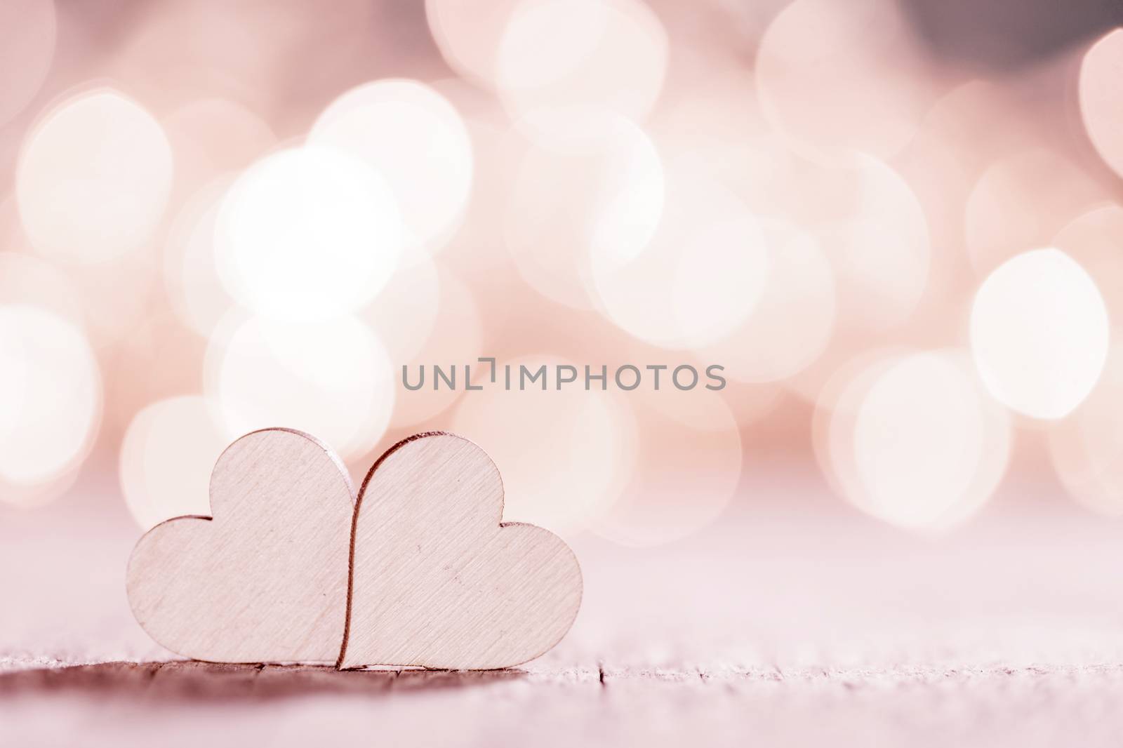 Two wooden hearts on pink glowing bokeh hearts background for Valentines day