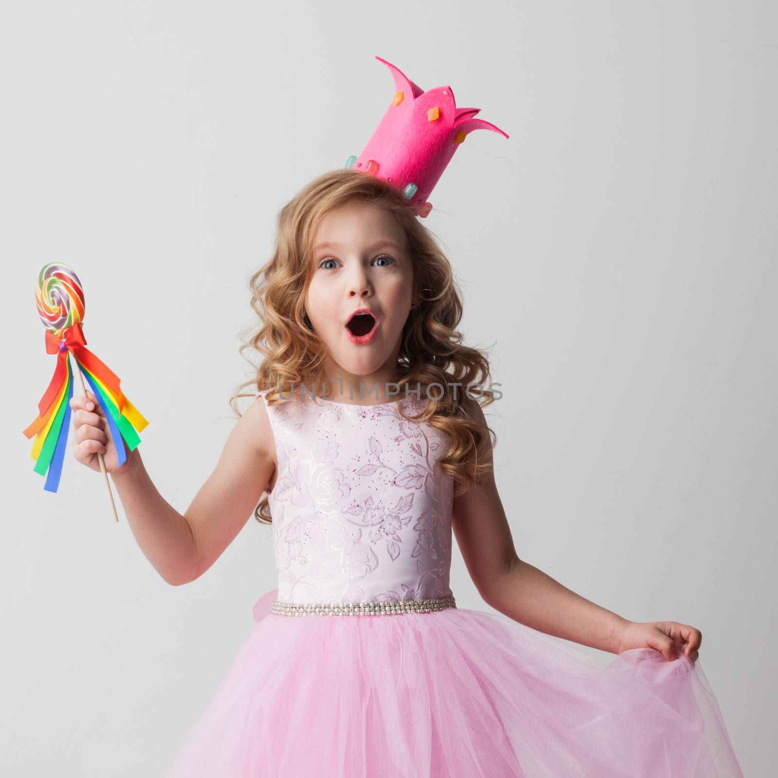 Beautiful little candy princess girl in crown holding big lollipop and smiling