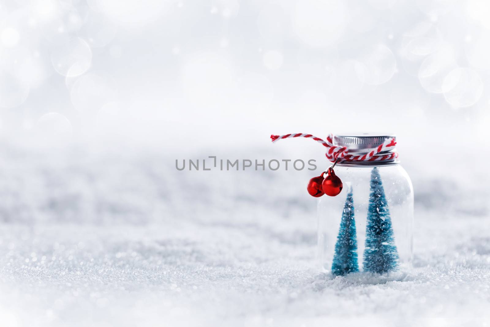 Christmas ornaments of glass jar with striped ribbon , bells and fir trees inside on snow background