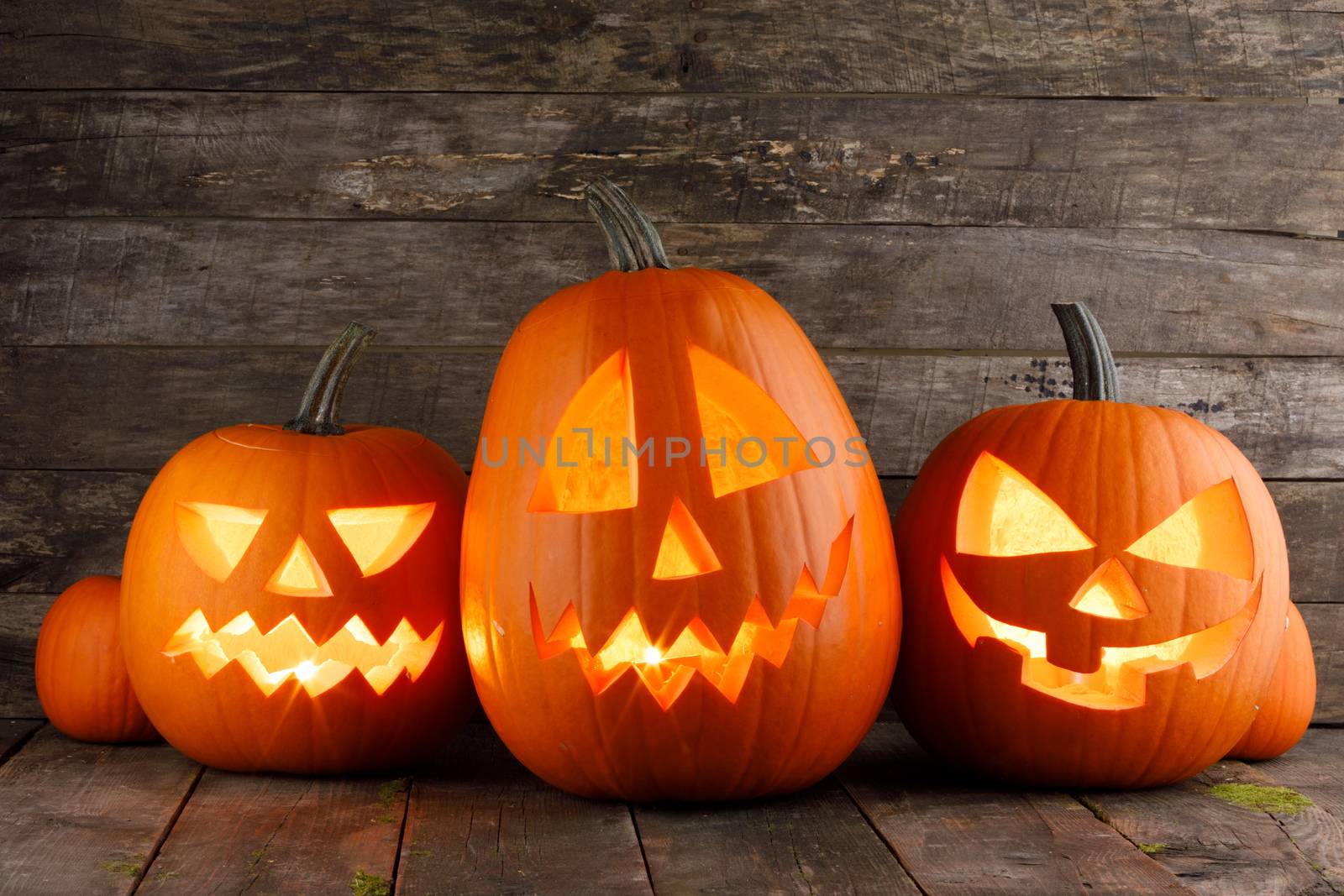 Three Halloween pumpkins head jack o lantern and candles on wooden table background