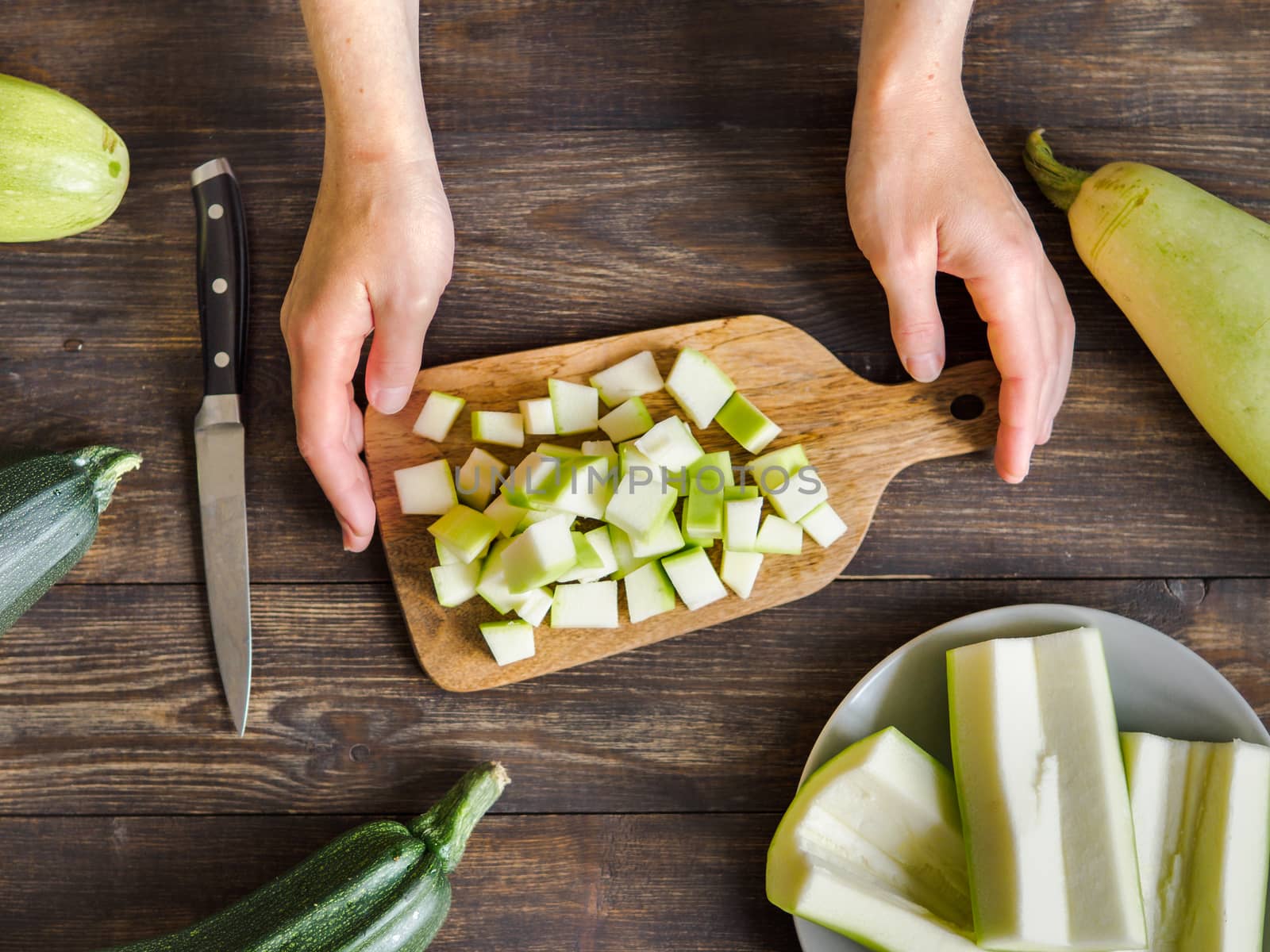 Zucchini harvest. Woman slices zucchini cubes for freezing on wooden table. Farm organic zucchini harvesting Top view or flat lay.