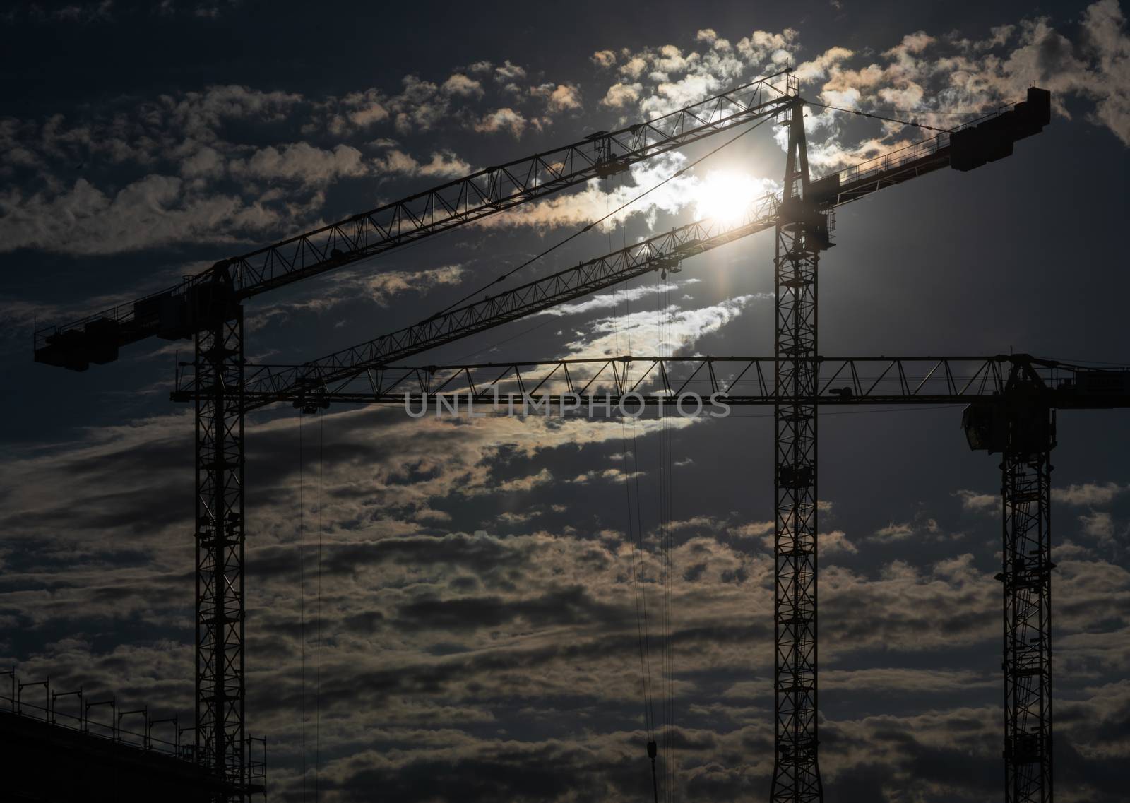 Cranes on a construction site with a cloudy sky during sundown