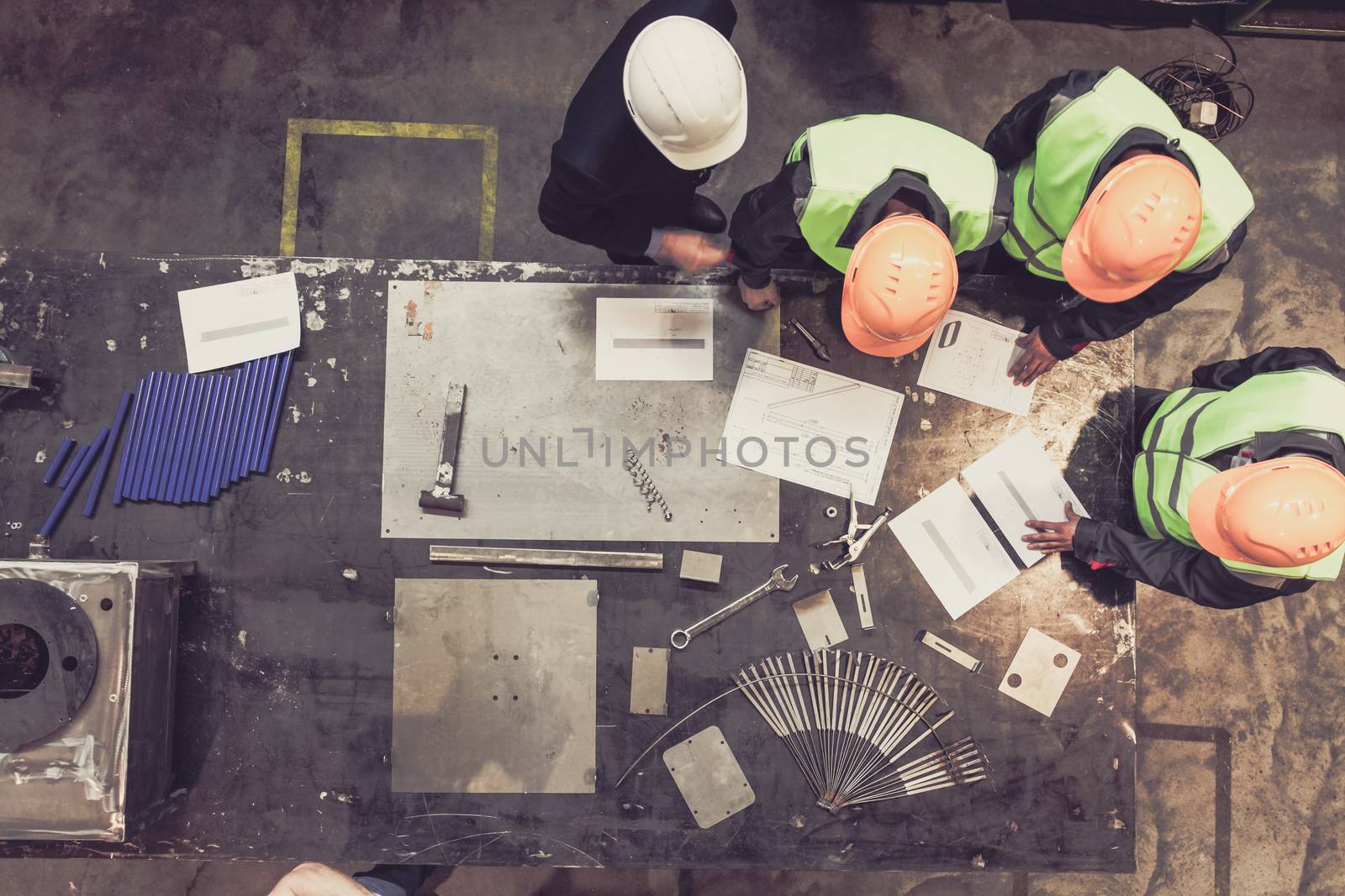 Workers and manager in safety helmets working with documents at factory