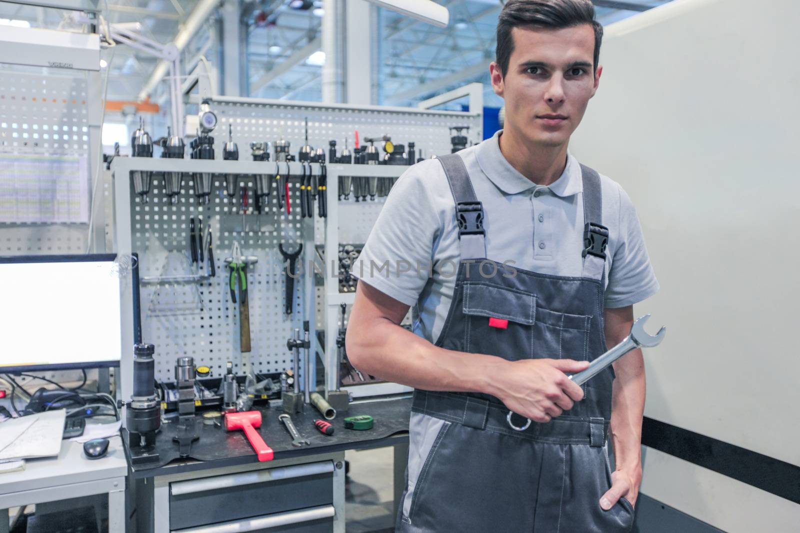 Portrait of a young worker holding wrench at workplace with computer and tools at CNC factory