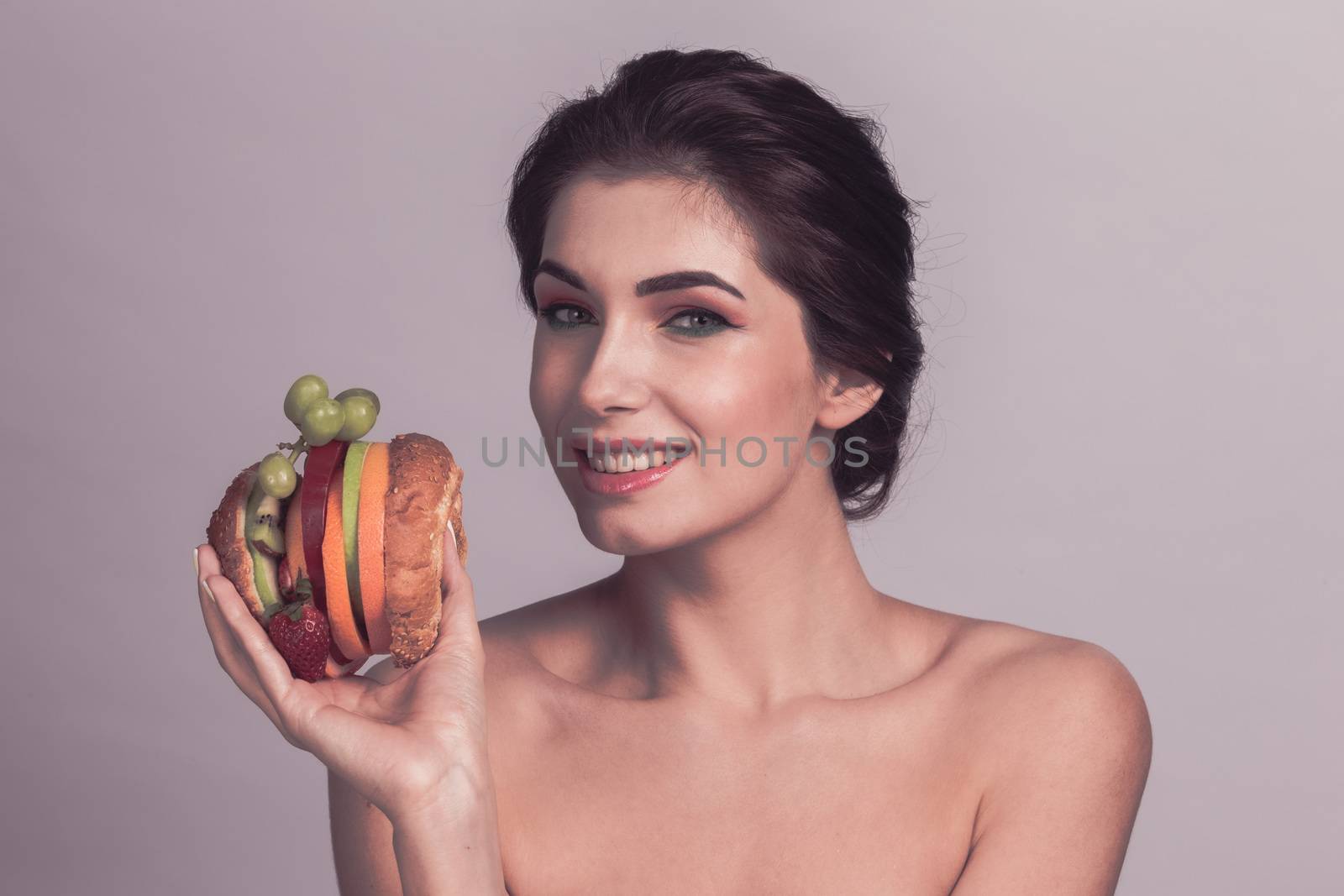 Portrait of beautiful woman holding vegan burger made of fruits