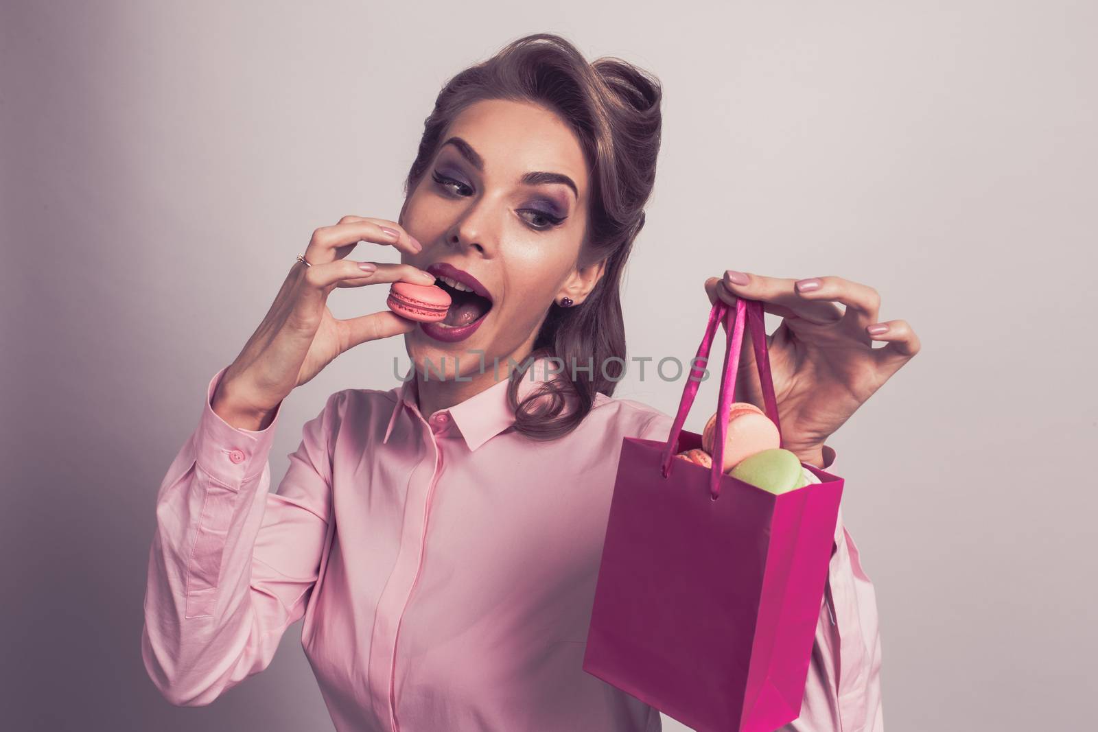 Funny smiling blond woman eating colorful macaroons