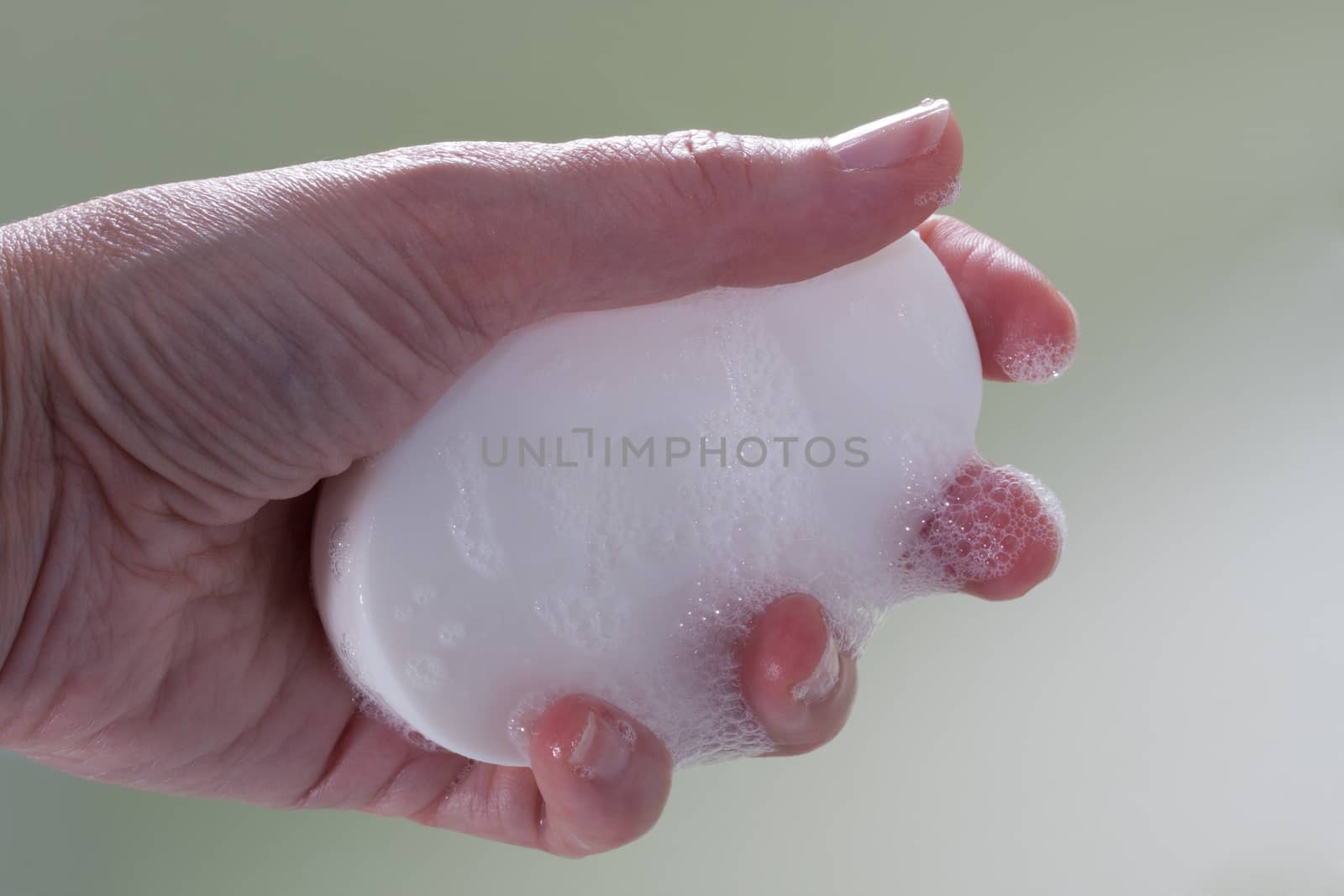 Female hand holding a web foamy soap bar, green background