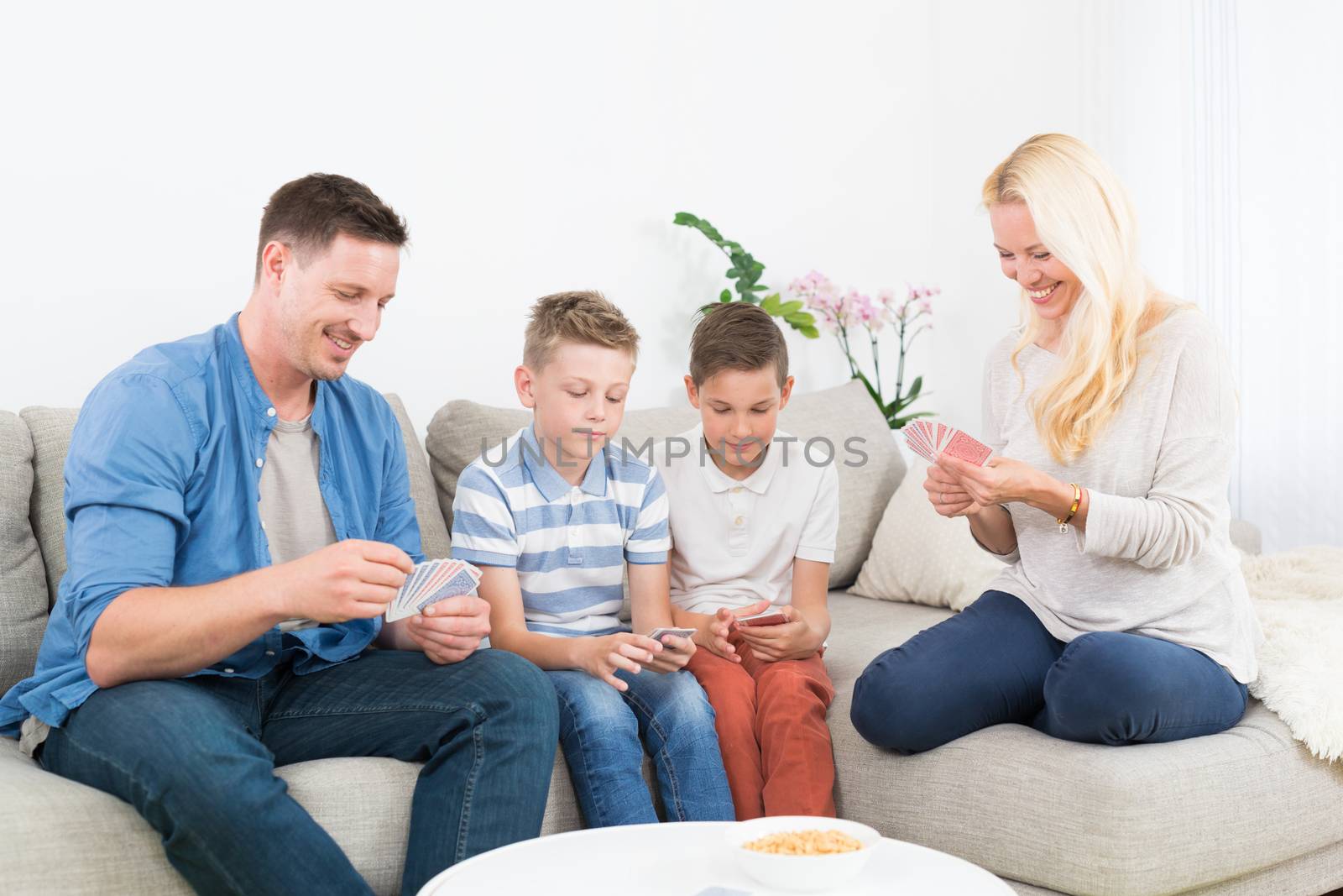 Happy young family playing card game on living room sofa at home. Spending quality leisure time with children and family concept.