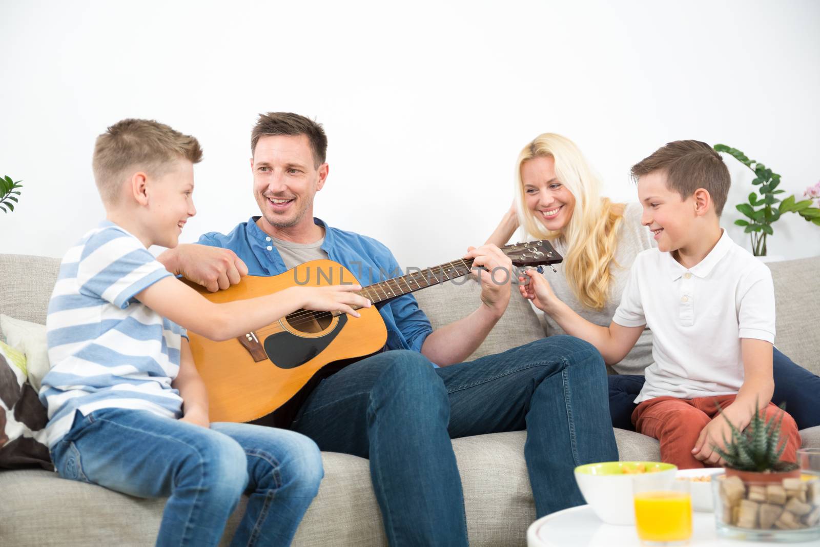 Happy caucasian family smiling while playing guitar and singing songs together at cosy modern home. Spending quality leisure time with children and family concept.