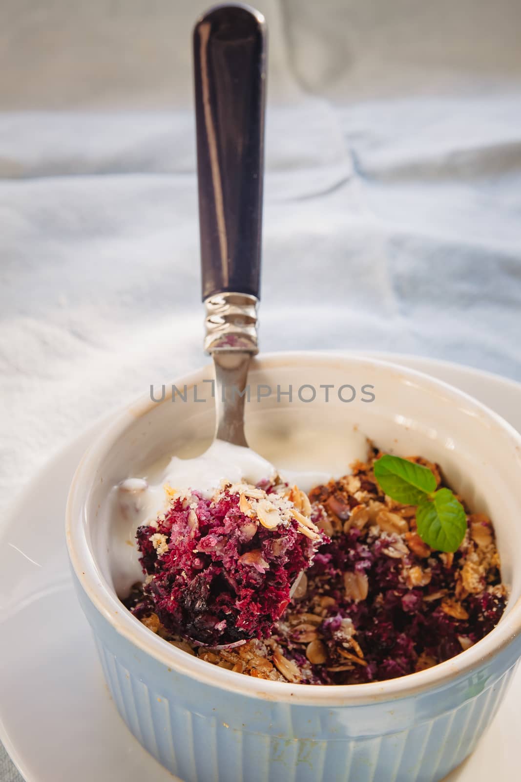 baked oat-blueberry crumble with mint in a white and blue plate on a rustic linen tablecloth. Save the space, top view. The concept of healthy proper nutrition for breakfast, vegetarianism