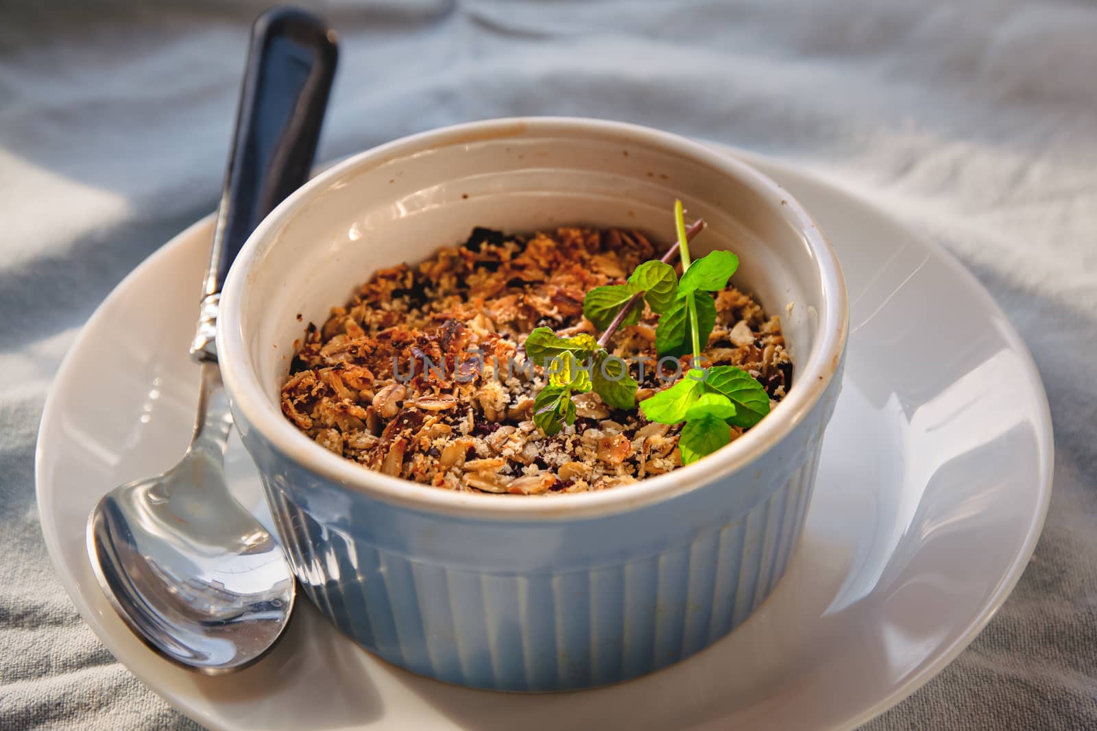 baked oat-blueberry crumble with mint in a white and blue plate on a rustic linen tablecloth. Save the space, top view. The concept of healthy proper nutrition for breakfast, vegetarianism