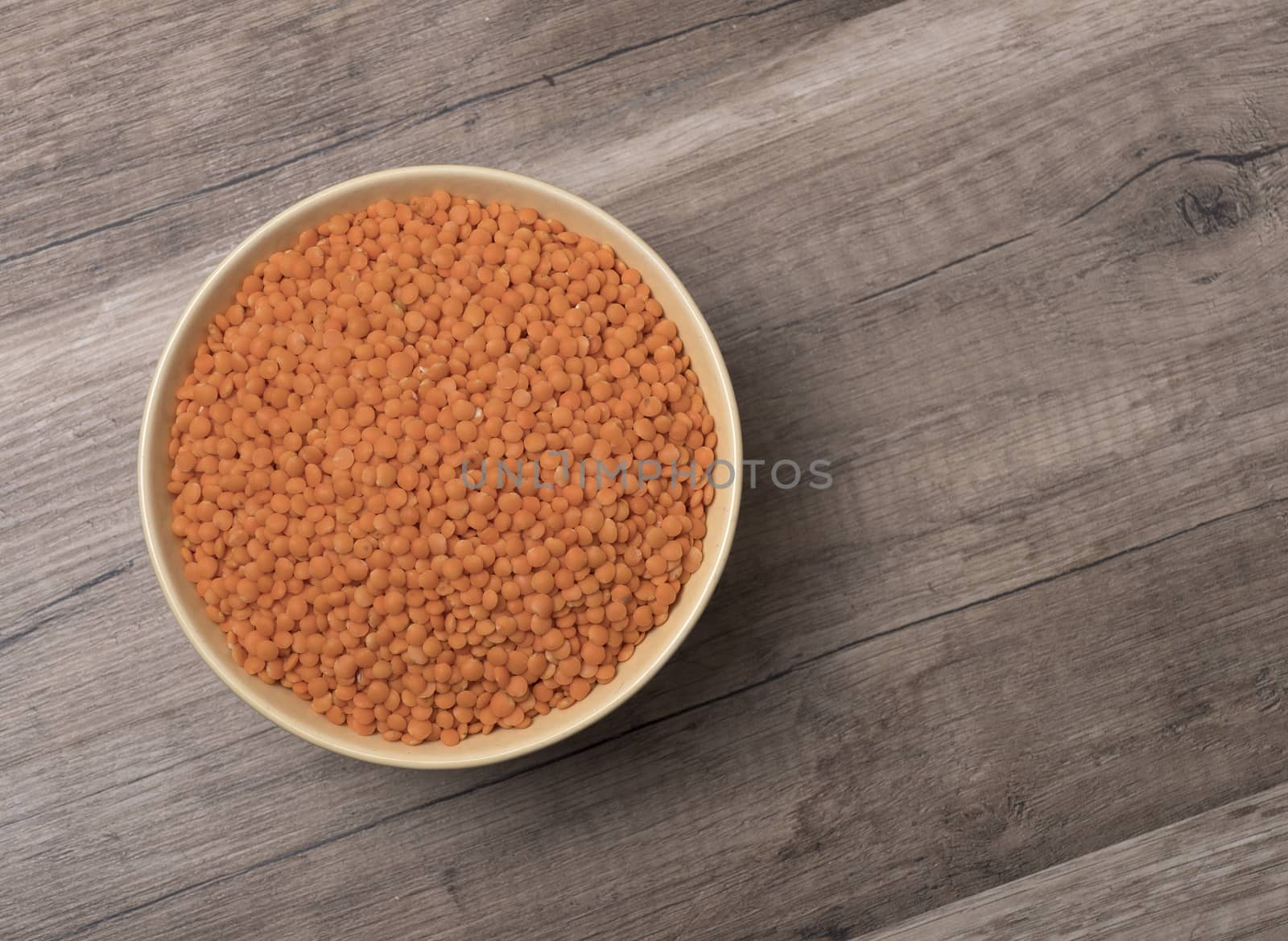 Dry red lentils in a bowl on wooden background. Top view.