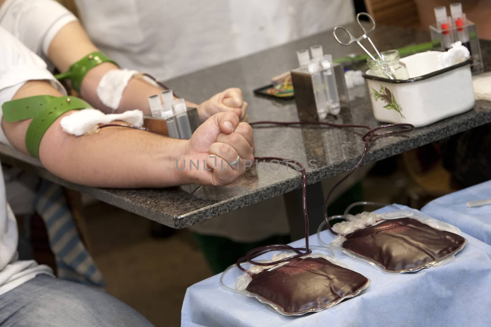   blood donation, hands with rubber tourniquet used in blood draw procedures. blood bags on the table 