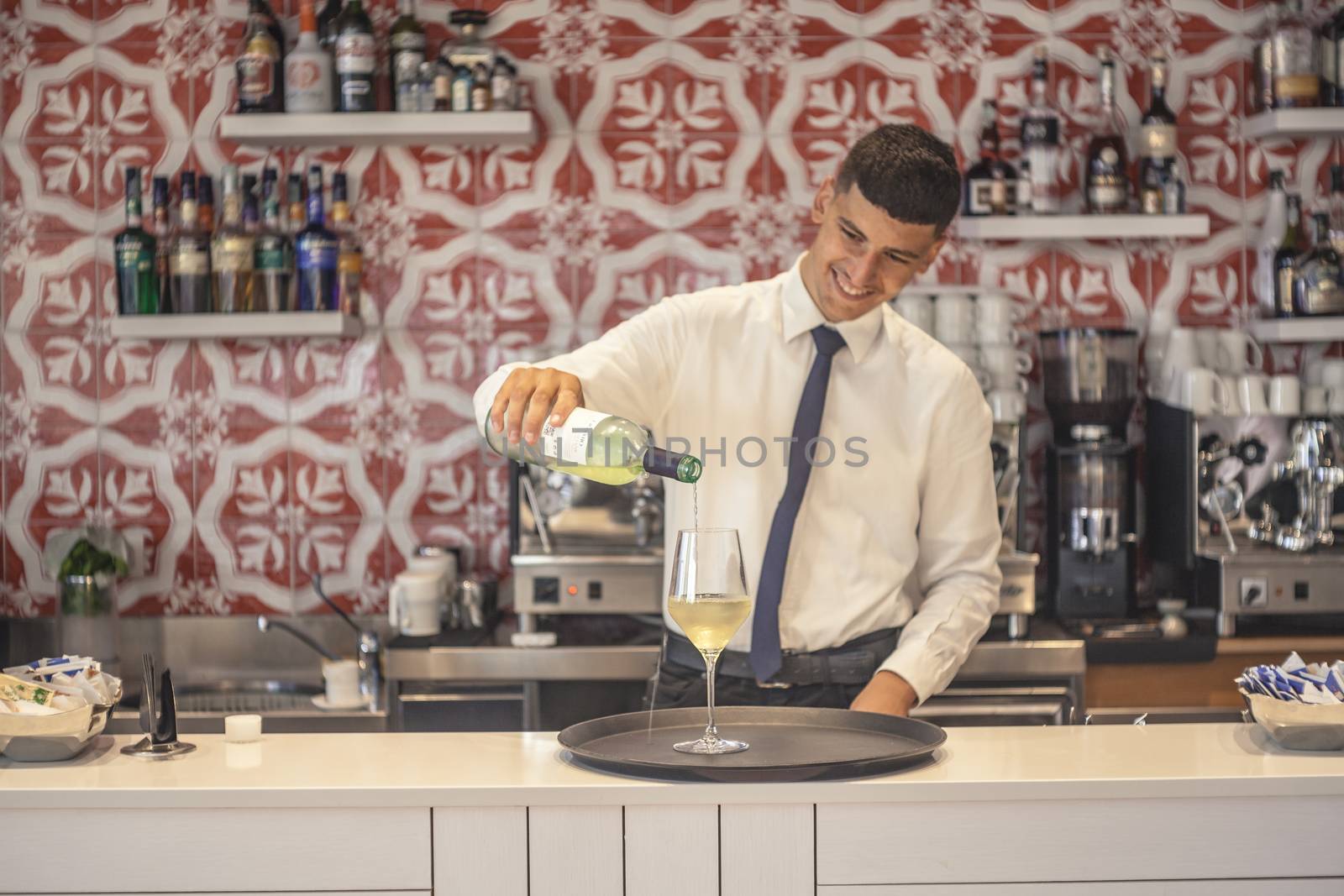 Barman in elegant suit pours wine behind the bar