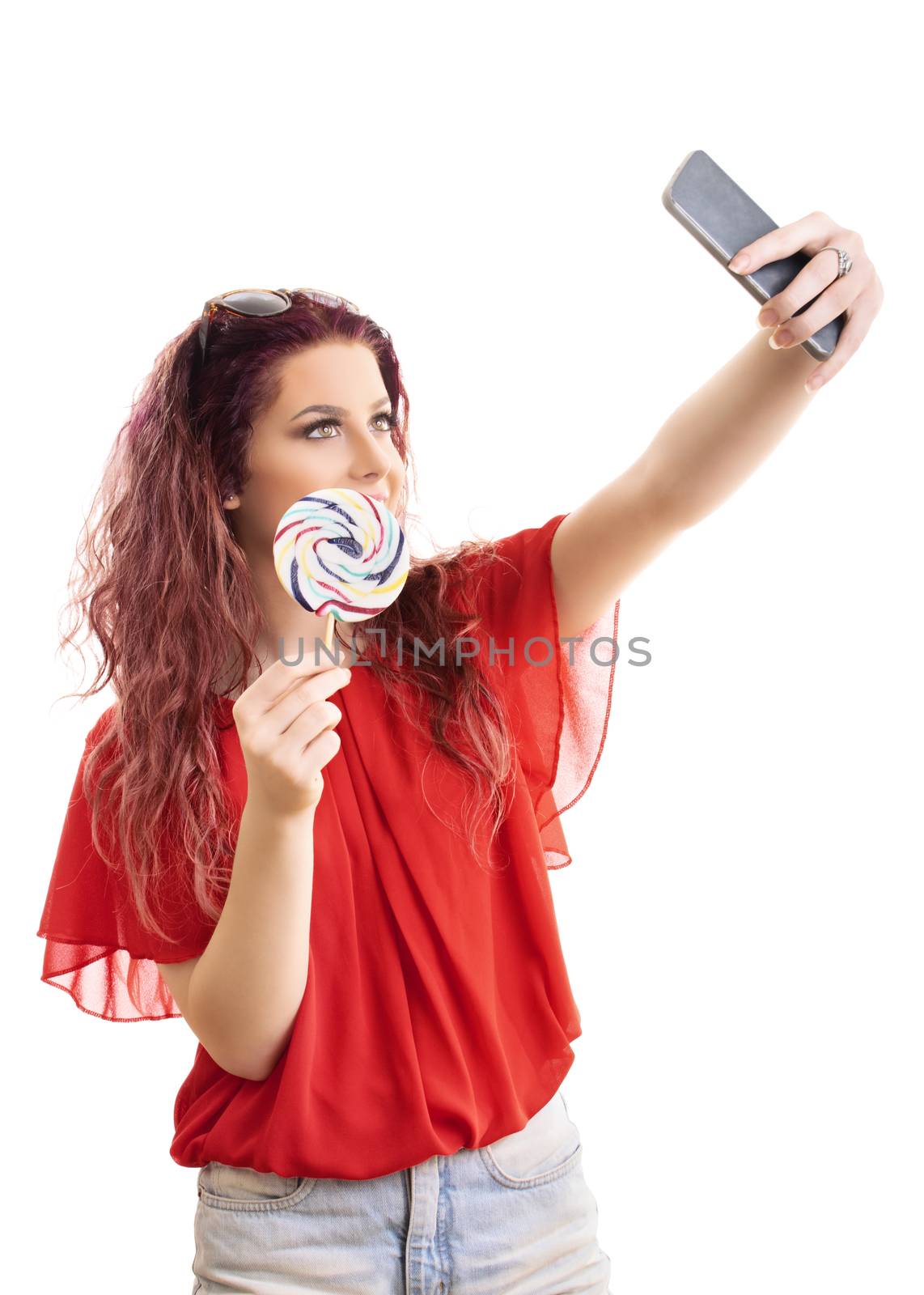 Beautiful fashionable young girl taking a selfie with a lollipop, isolated on white background.