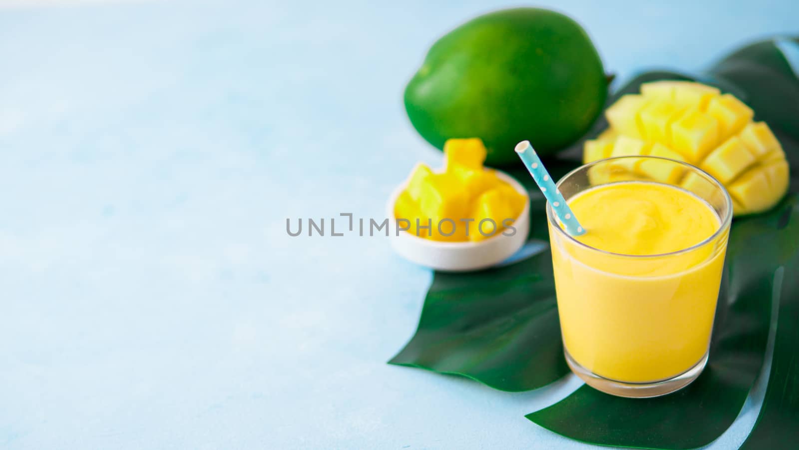 Yellow mango yogurt or smoothie on blue background with copy space left. Turmeric Lassie or lassi in glass. Banner