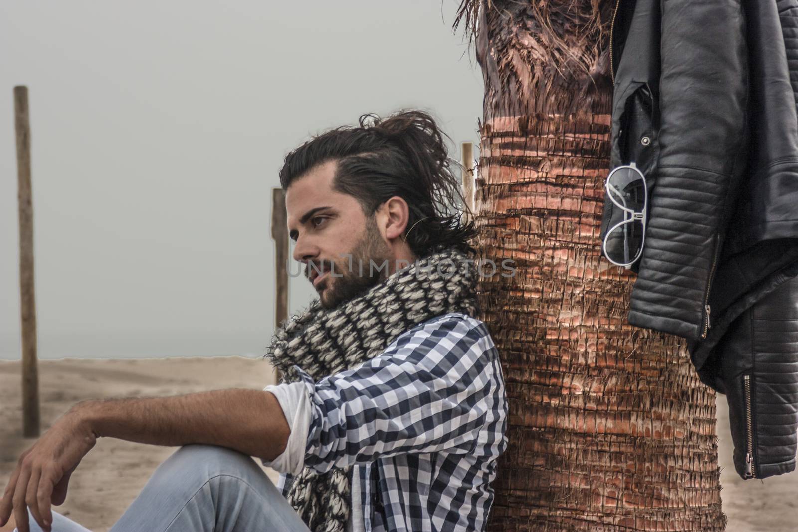 Fashion guy sitting by the sea near a palm