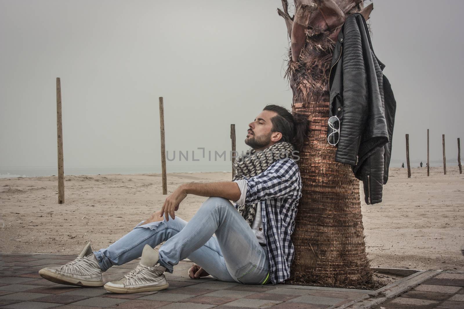 Fashion guy sitting by the sea near a palm