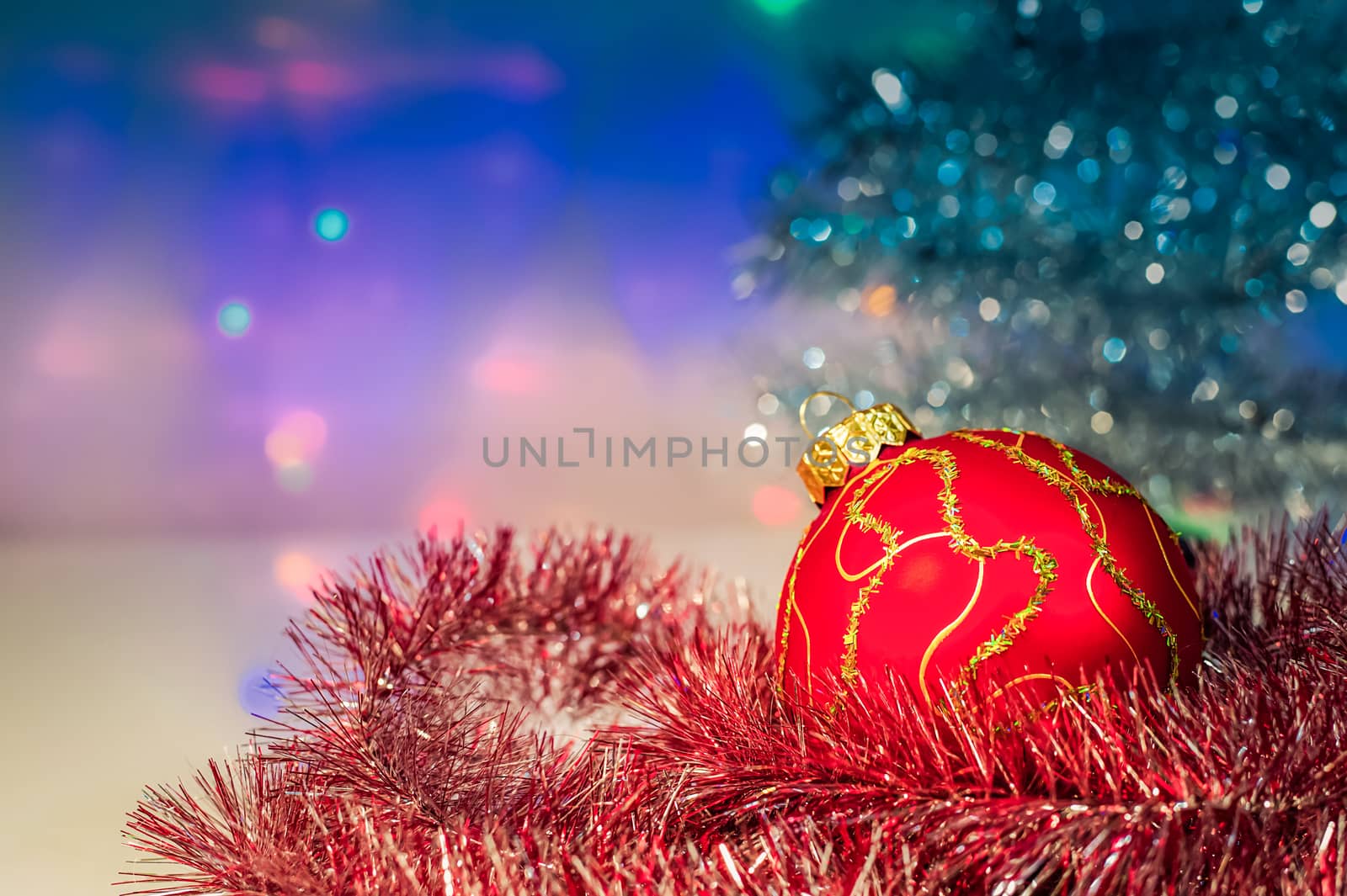 Red Christmas ball under the tree and tinsel on the background lights
