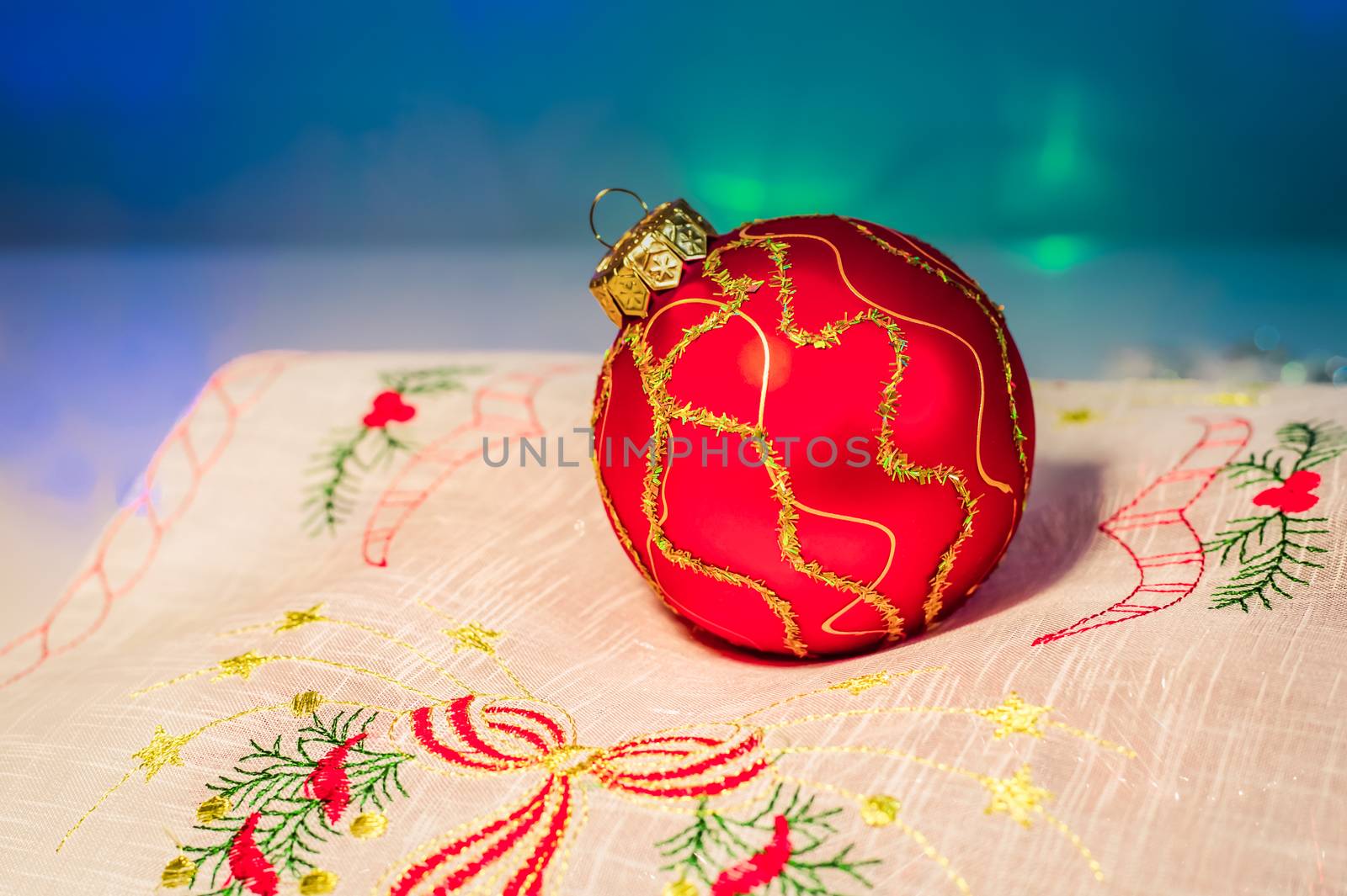 Red Christmas ball on festive napkin with embroidery on blue background