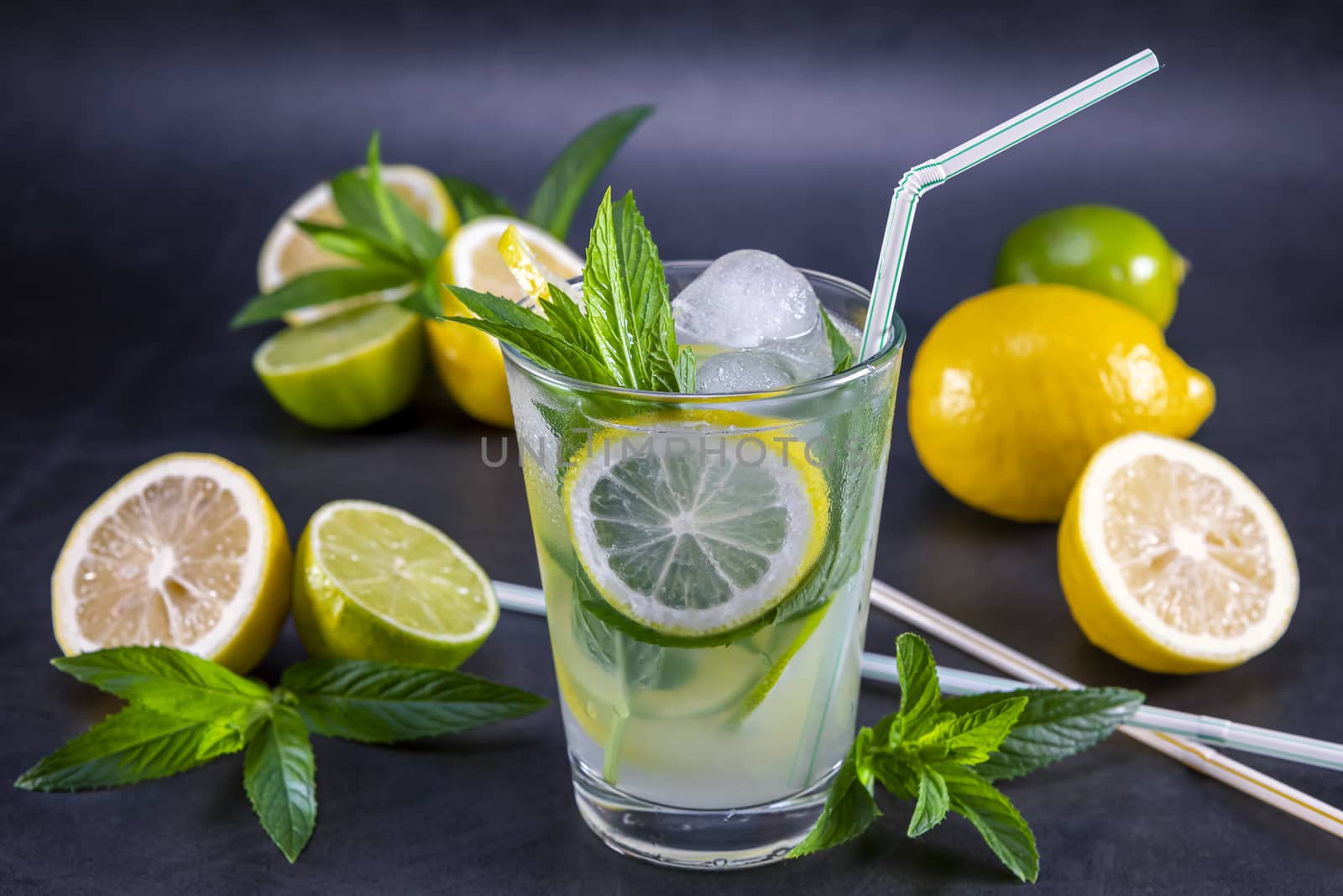 Cold refreshing summer lemonade with mint in a glass on a grey and black background. Focus on leaf in glass.