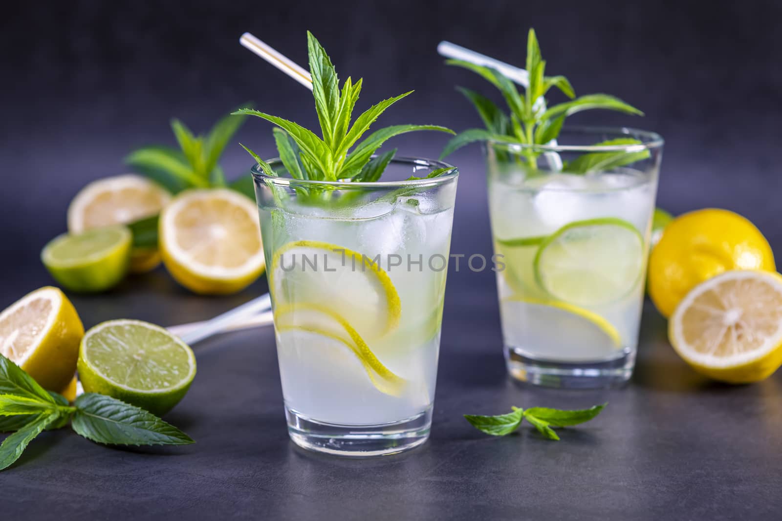 Cold refreshing summer lemonade with mint in a glass on a grey and black background. Focus on glass.