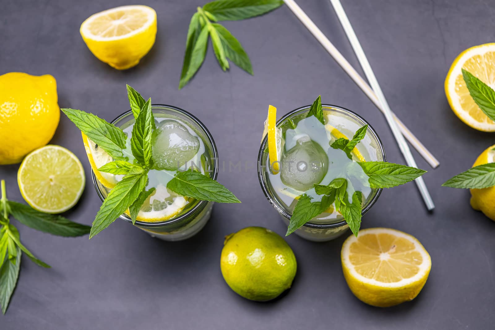 Top view of fresh lemonade with mint and ice in glasses on black background. Focus on leaf and ice.