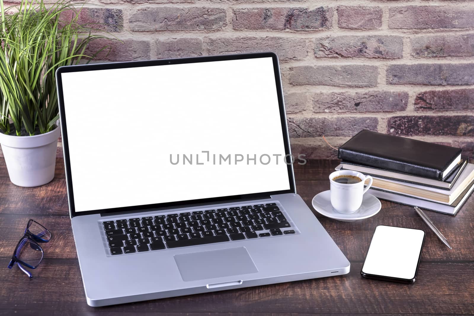 Laptop notebook with blank screen and cup of coffee and notepad pen and books and smart-phone on wooden table. 
Mock up on wooden table with laptop with blank screen, cup of coffee, pen, books and flower.
Focus on keyboard.