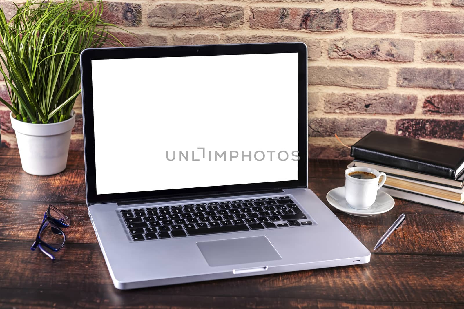 Laptop notebook with blank screen and cup of coffee and notepad pen and books on wooden table. 
Mock up on wooden table with laptop with blank screen, cup of coffee, pen, books and flower.
Focus on keyboard.