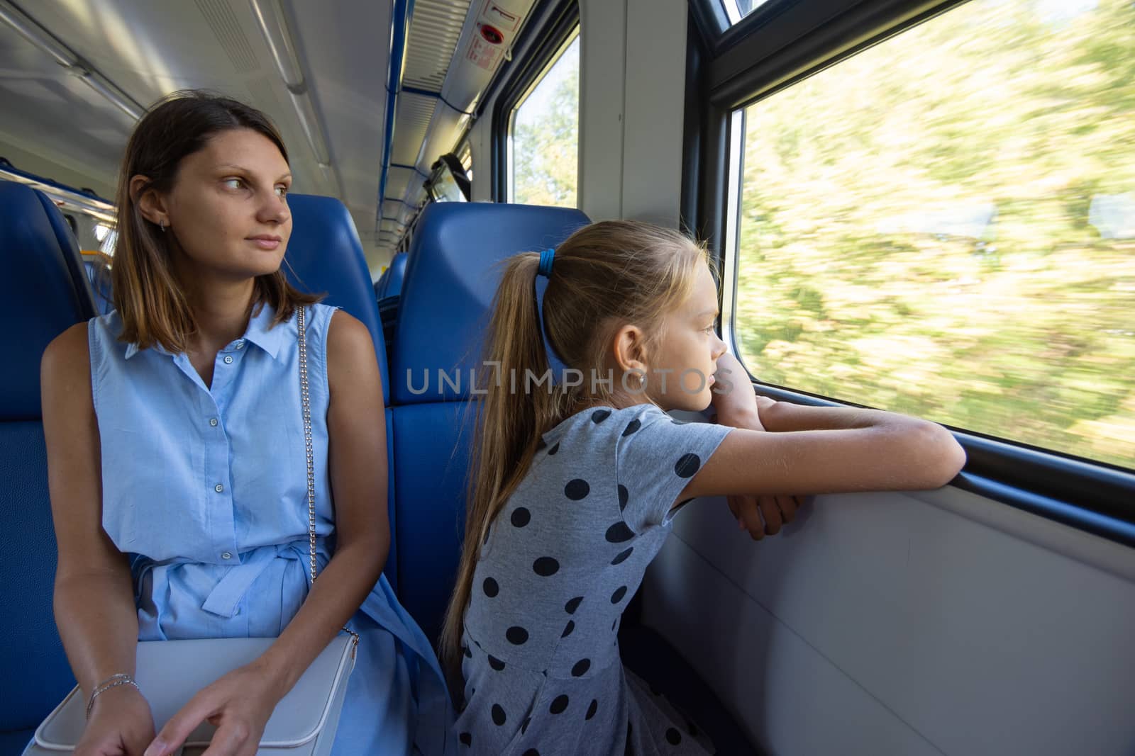 Mom and daughter in an electric train car, look out the window with enthusiasm