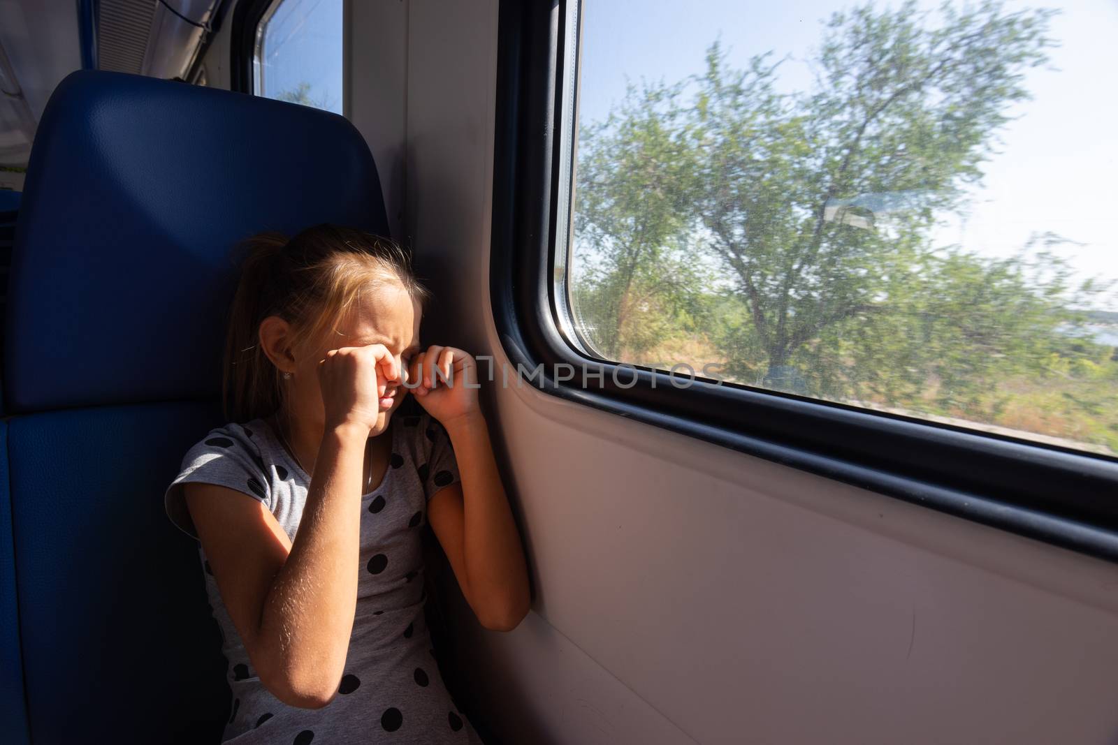 A girl rubs her eyes from the sun in an electric train car