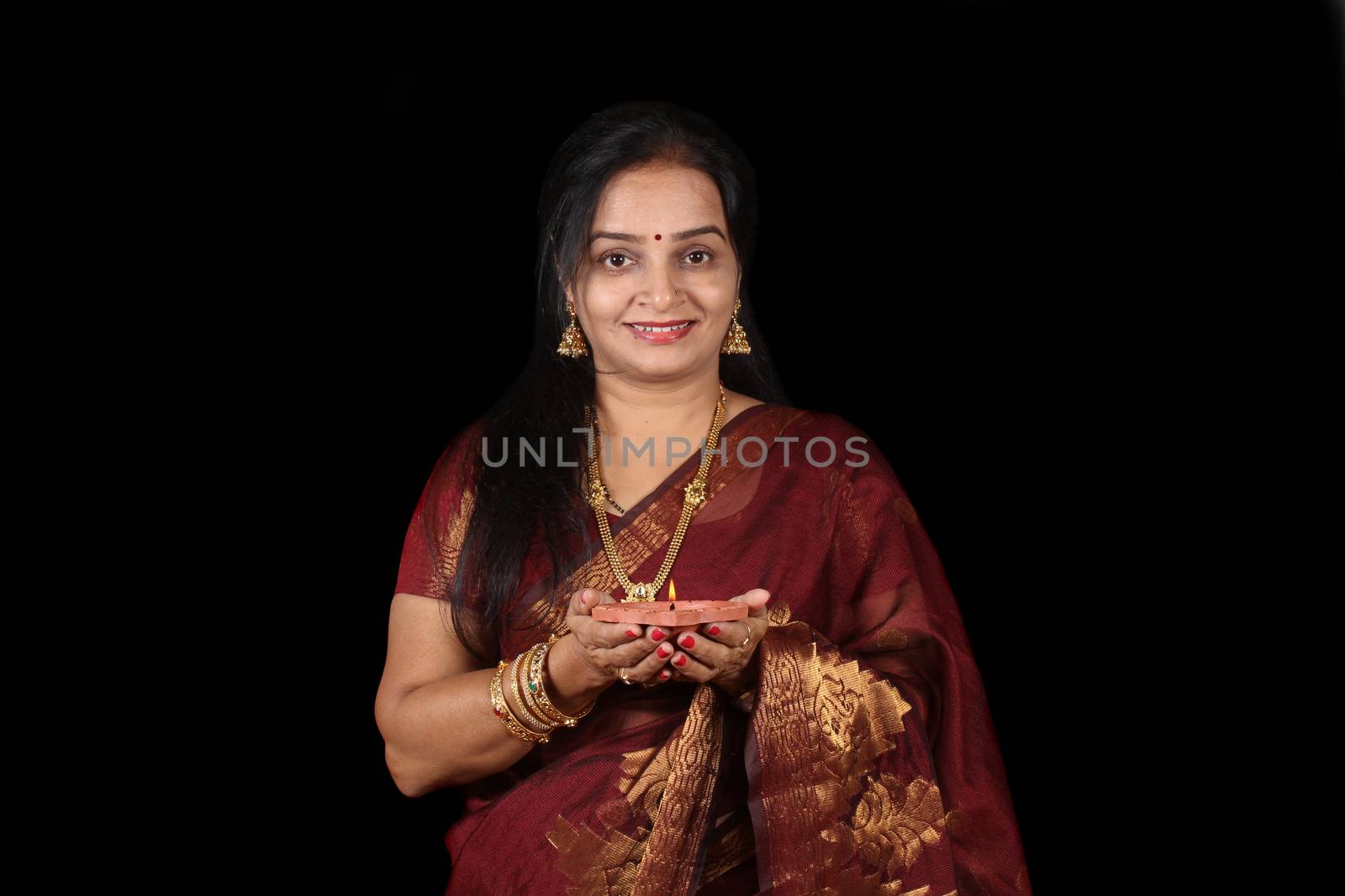 A beautiful middle aged Indian woman holding a lamp in her hand, on black studio background.