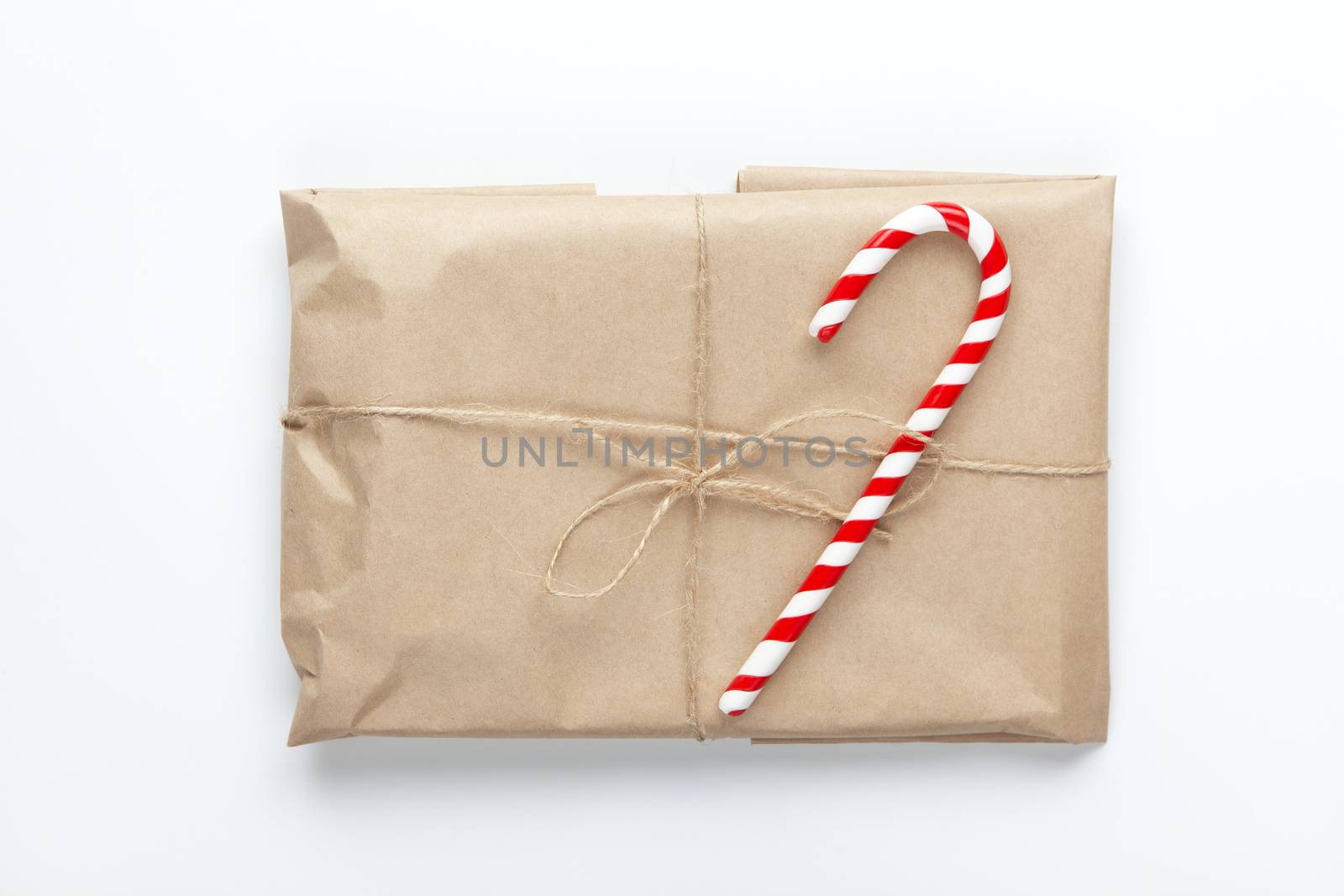 Christmas gift wrapped in craft paper, tied with scourge, decorated with cane candy on white background. Simple minimal style. Flat lay. Top view. Do it yourself, celebration concept.
