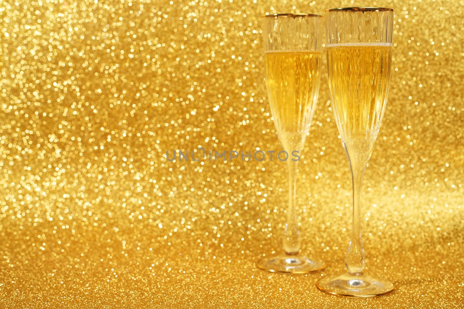 Two glasses of champagne with golden glitter lights on background