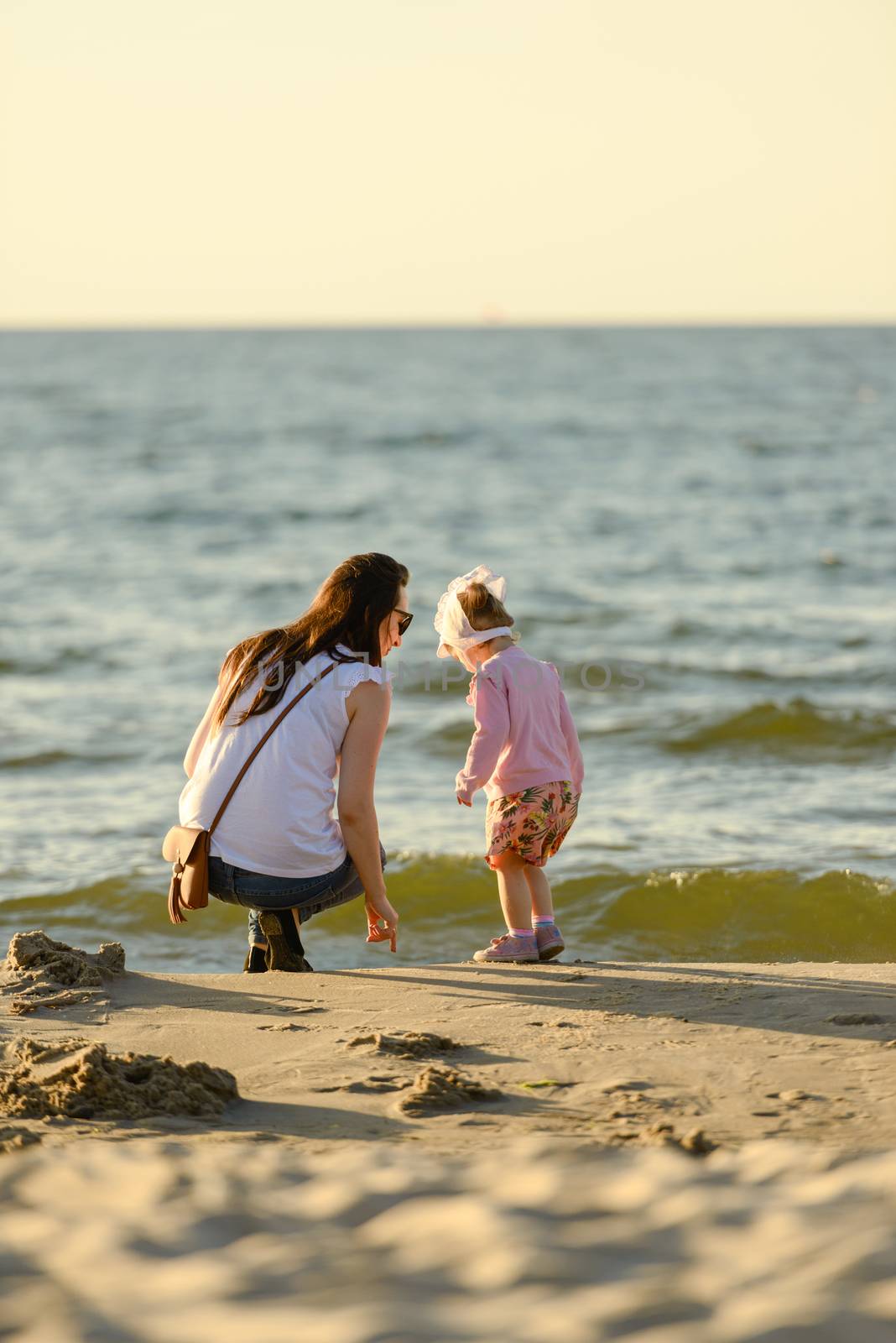 Mother and little daughter playing on the beach. Authentic image.