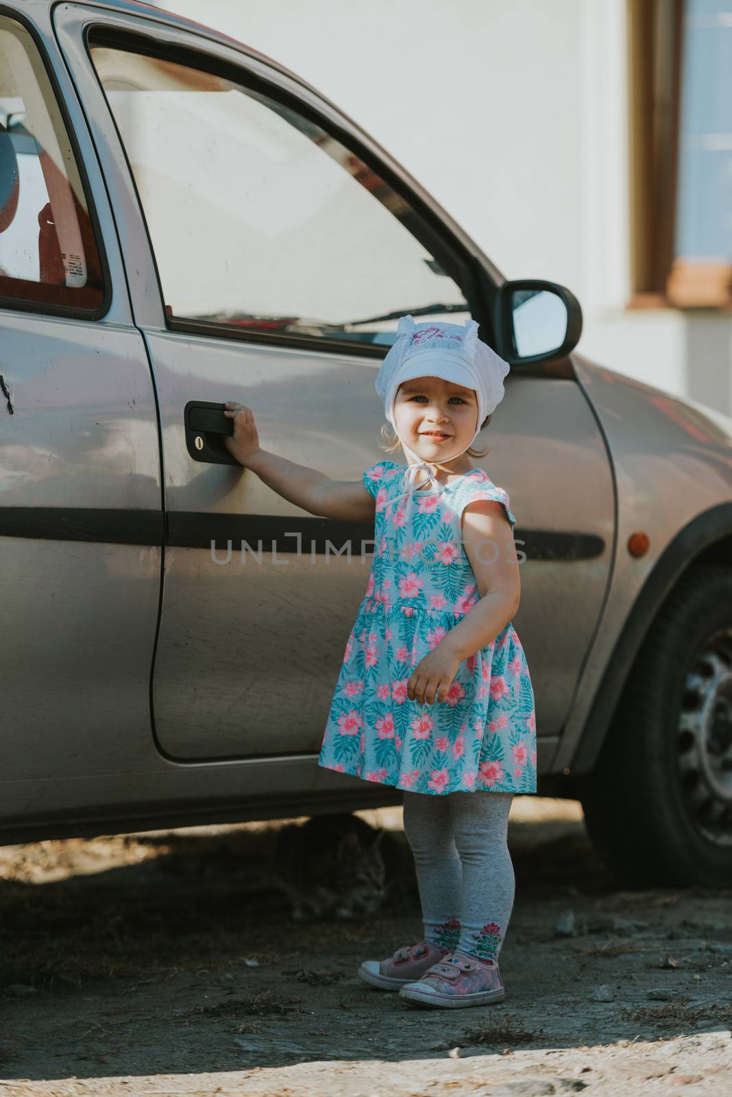 portrait of a little girl with a cat. Play. Cat is hiding under the car