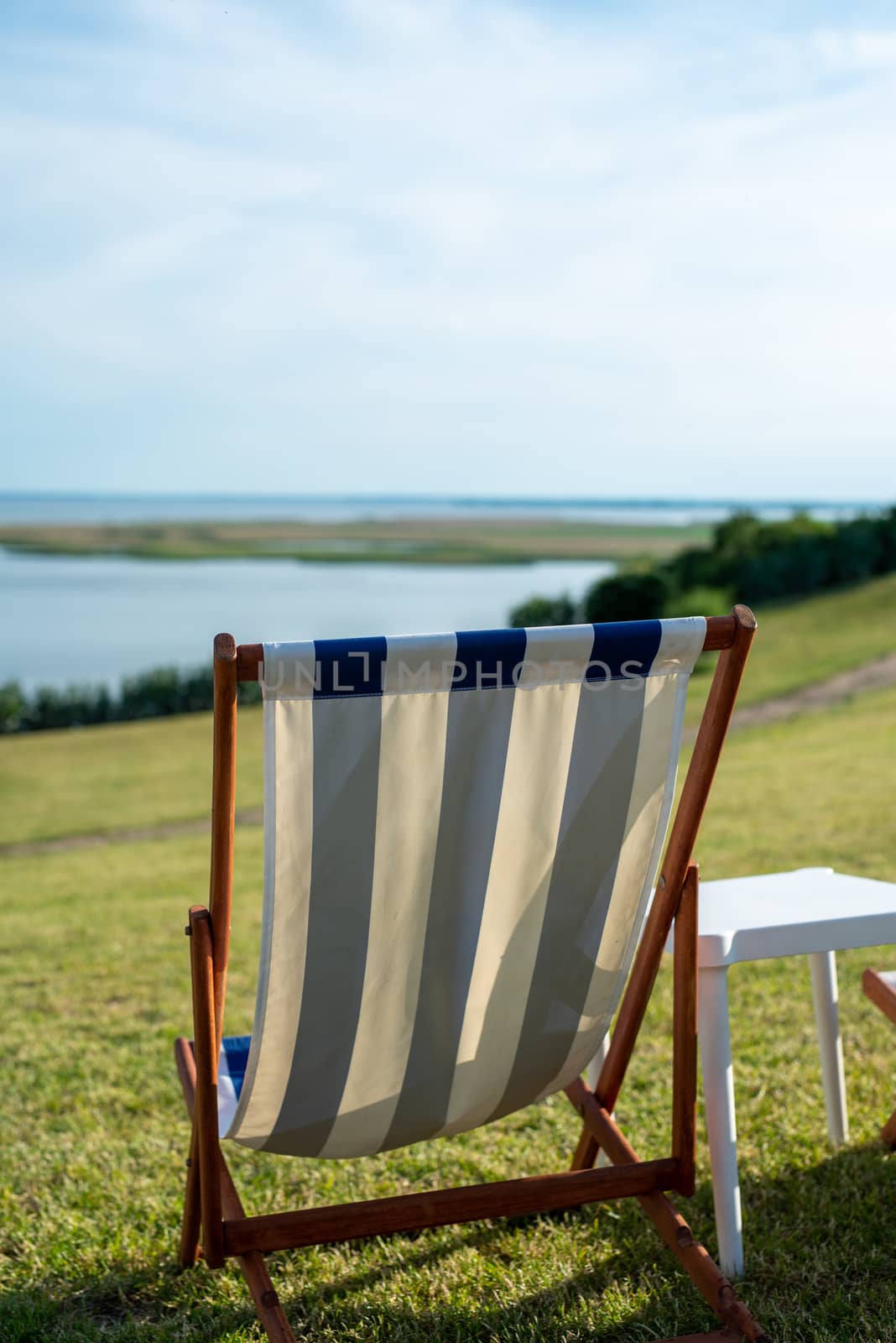 Empty beach chair on meadow on summer time. Sunlight and sea in the background. Coast line