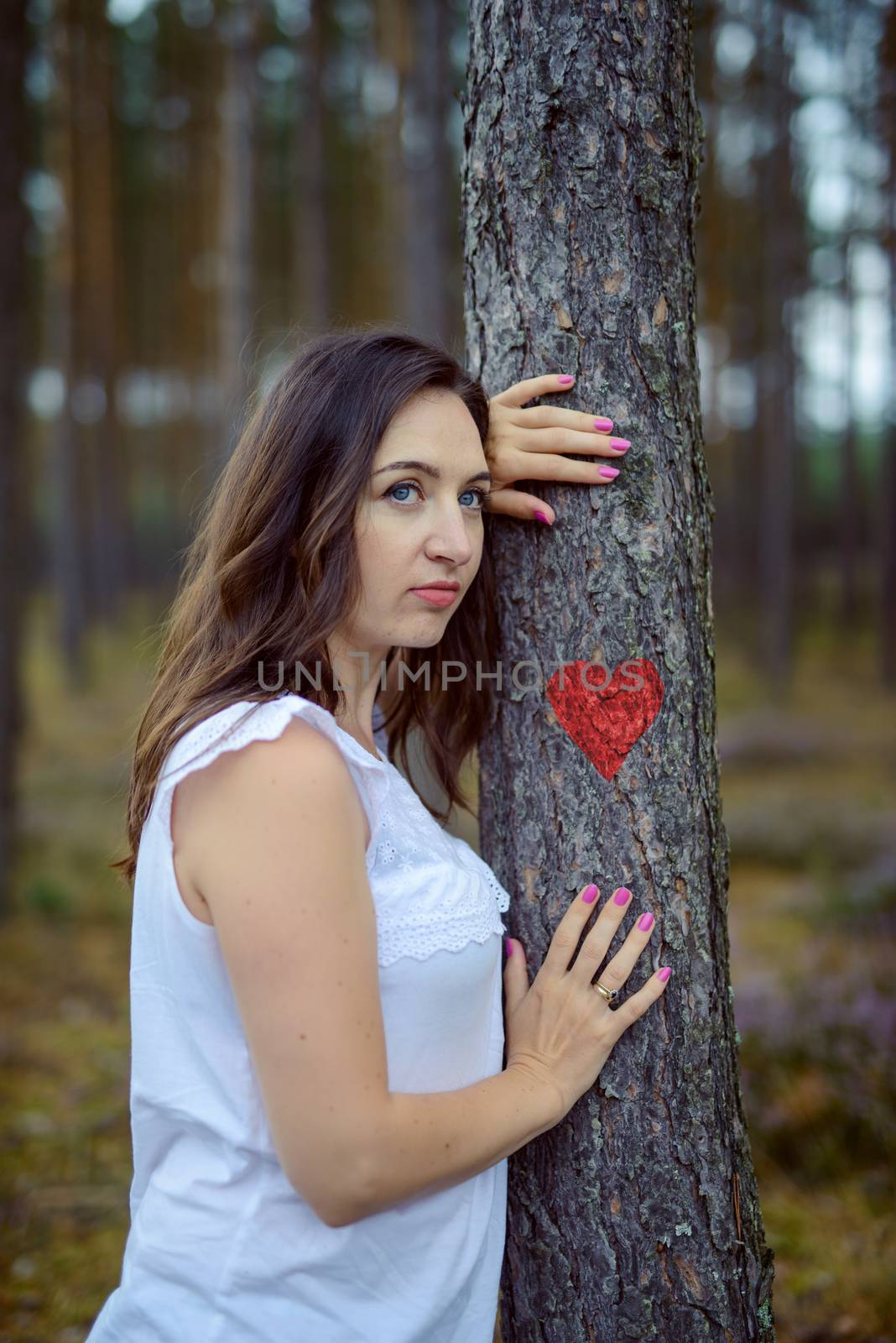 young woman holds hands on a tree on which a red heart is painted. love of nature. copy space. authentic image.