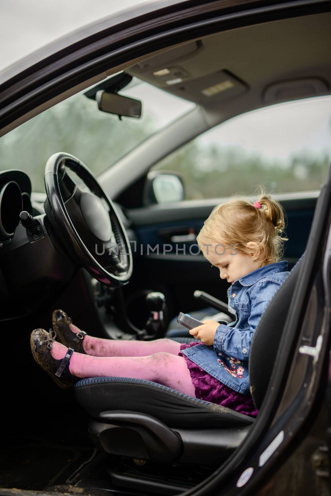 Little girl in a car seat. Holding phone in her hand. Taking driver seat. Car damage. Authentic image.