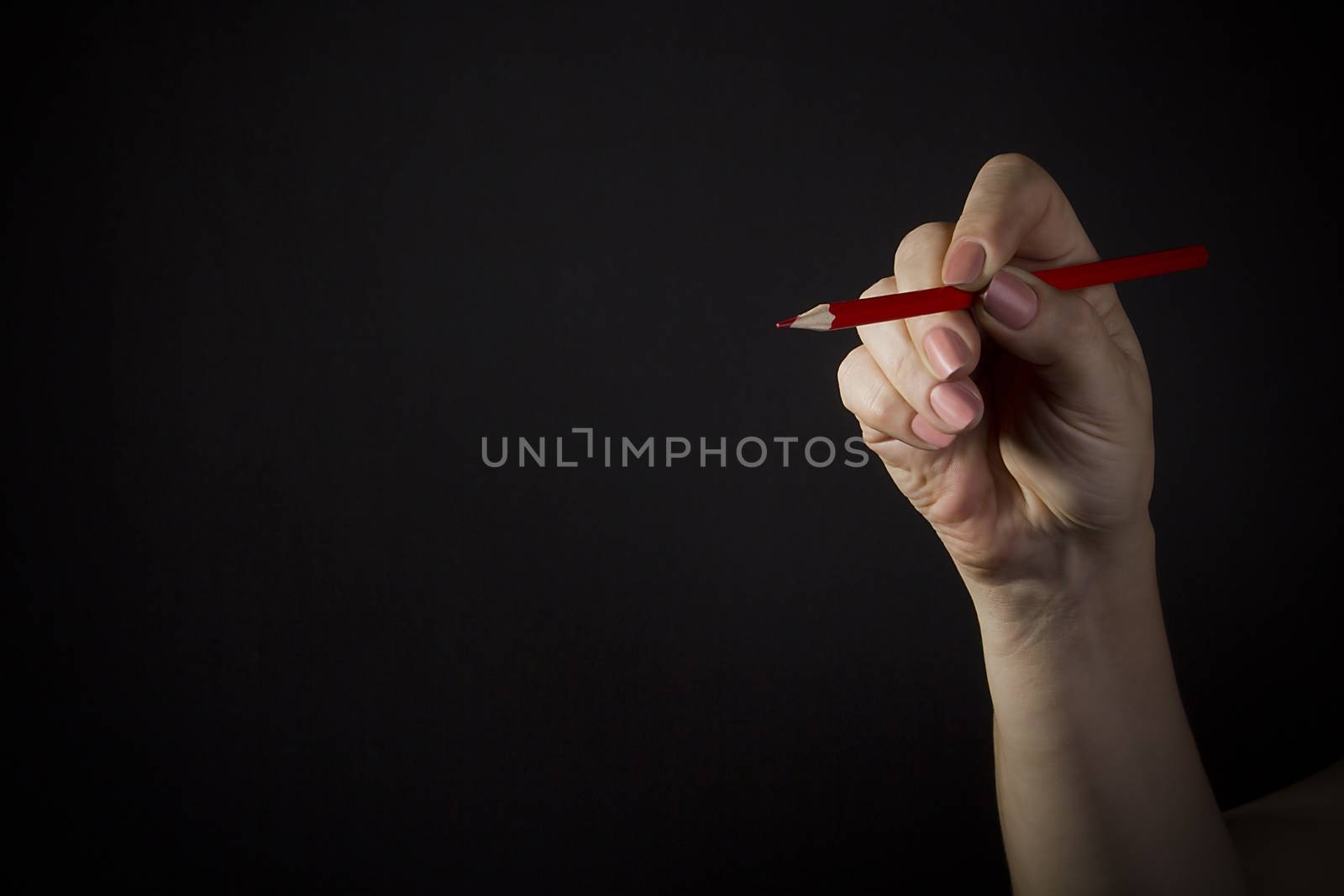 Female hand with a red pencil on a black background