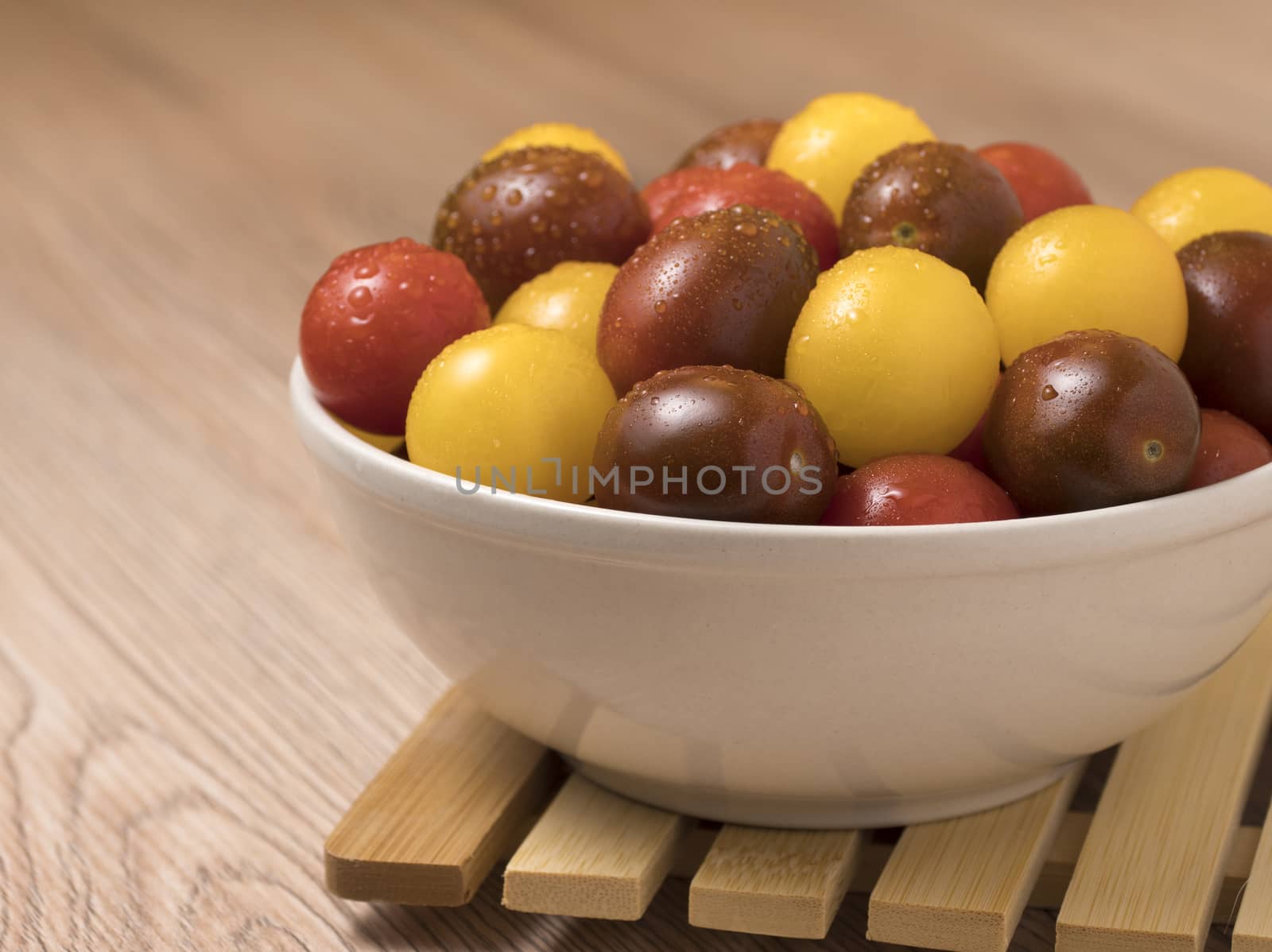 Cherry tomatoes in a variety of colors in ceramic bowl on wooden background.