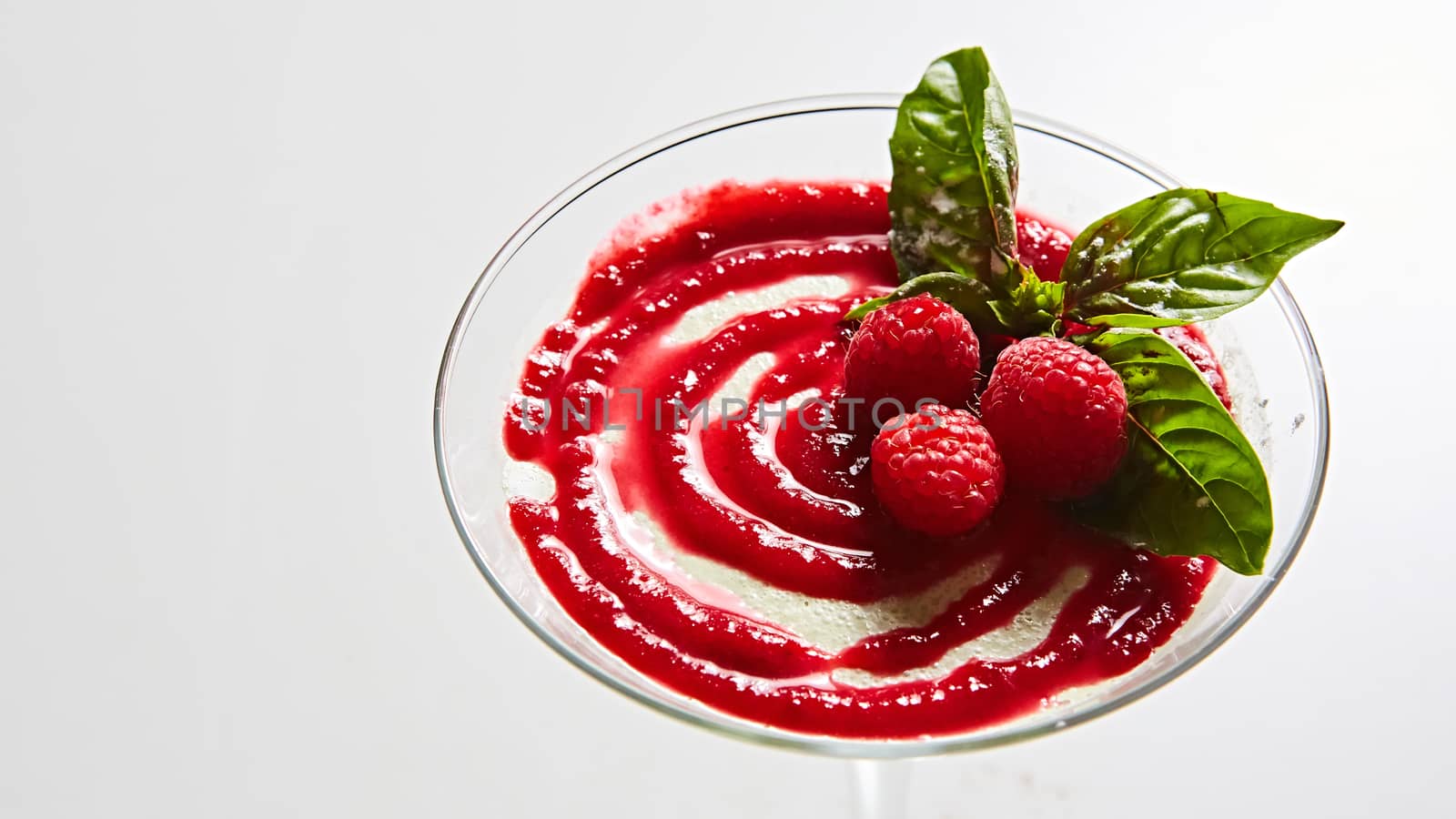 Delicious Italian dessert Panna Cotta with raspberry in small transparent glass.