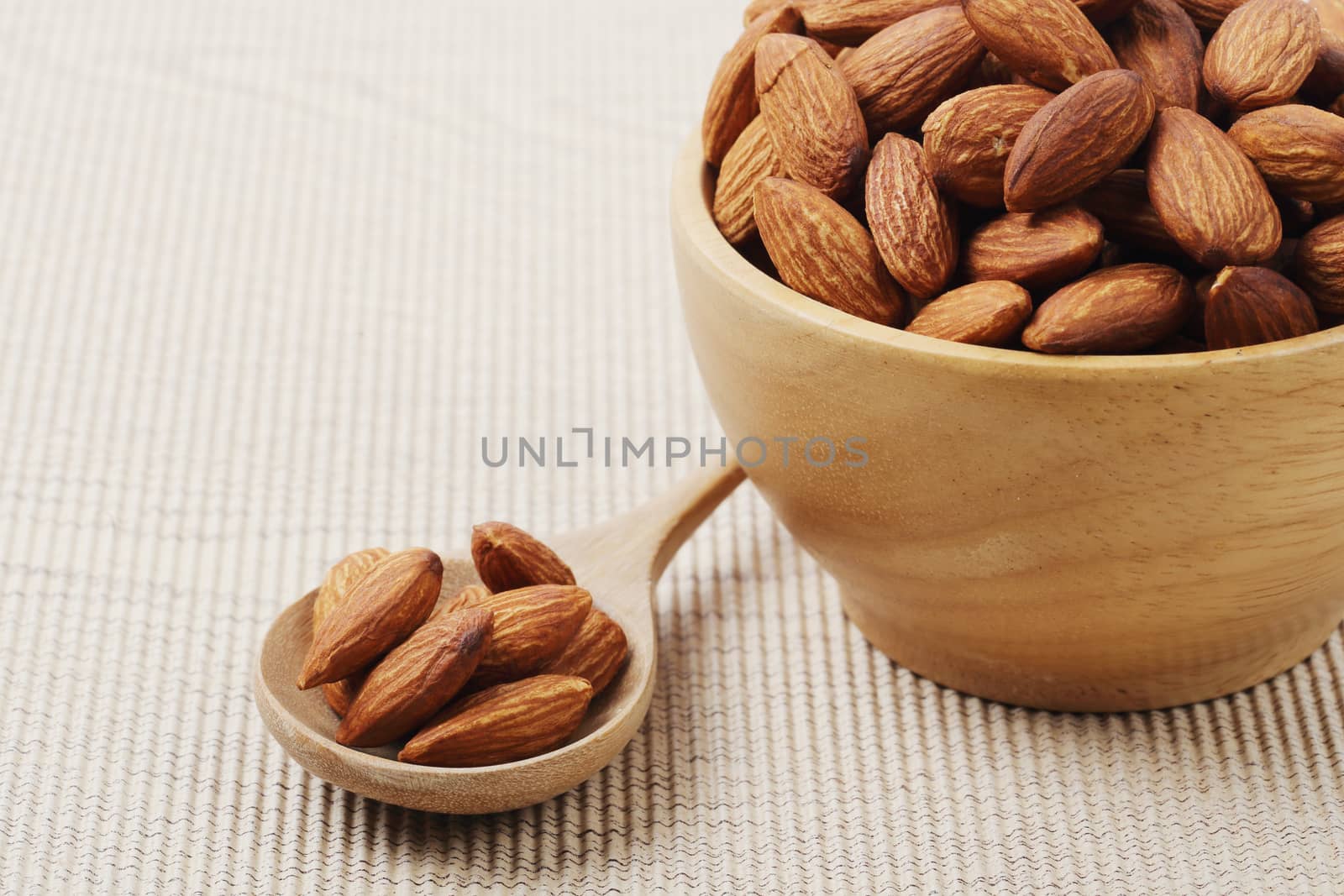 Close of dry almonds nuts in a wooden spoon over corrugated paper background.