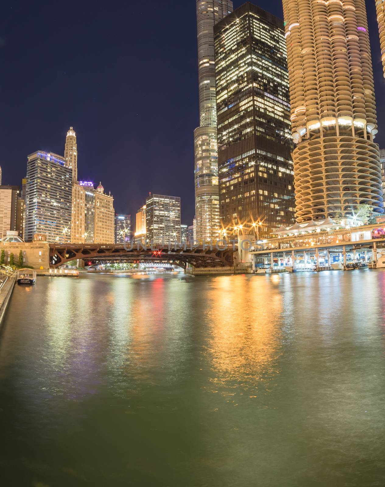 View from large fishing pier on Marina Cove toward riverside Chicago skylines and State Street at blue hour