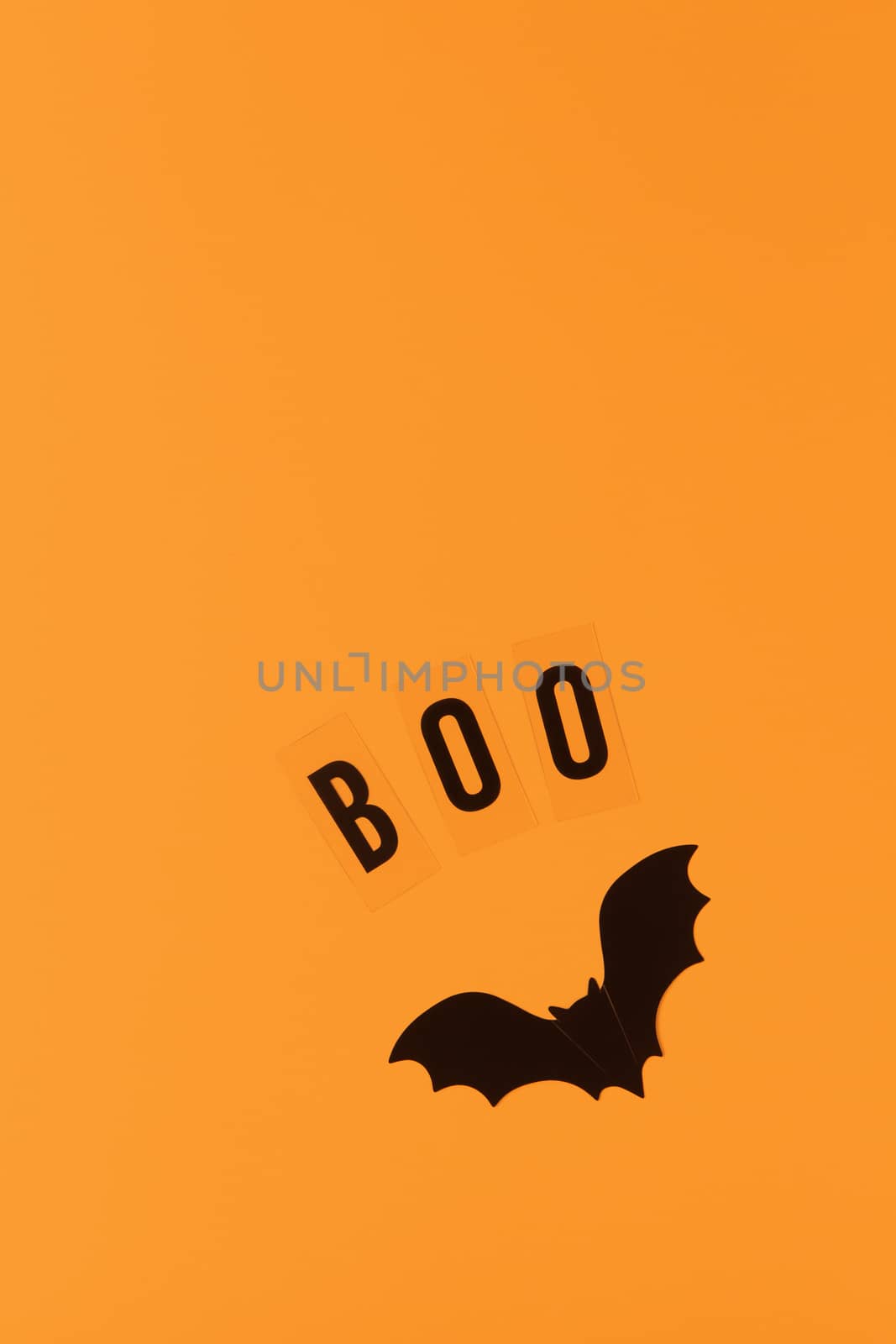 Halloween holiday flat lay. Black plastic bat and inscription Boo on orange background, copy space. Minimal style. Vertical. Trick-or-treat concept.