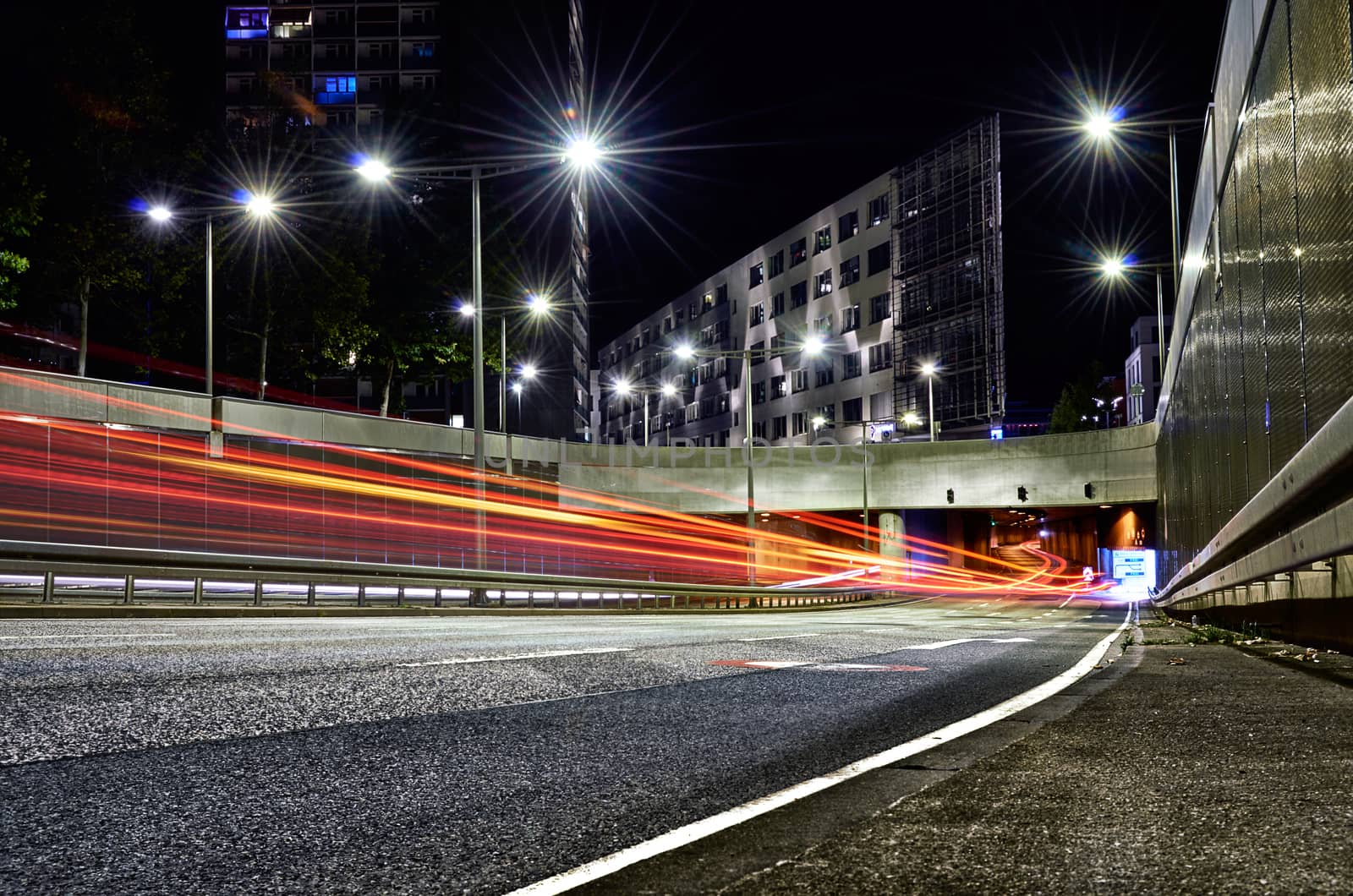 Tunnel opening in city with car trails surrounded by asphalt and concrete with modern buildings