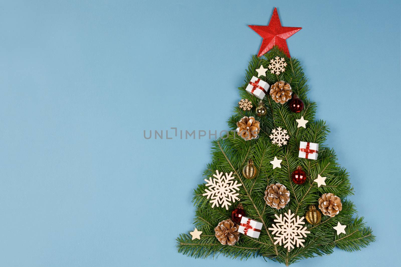 Christmas tree made of natural spruce branches deecor with red star on blue background, flat lay card with copy space