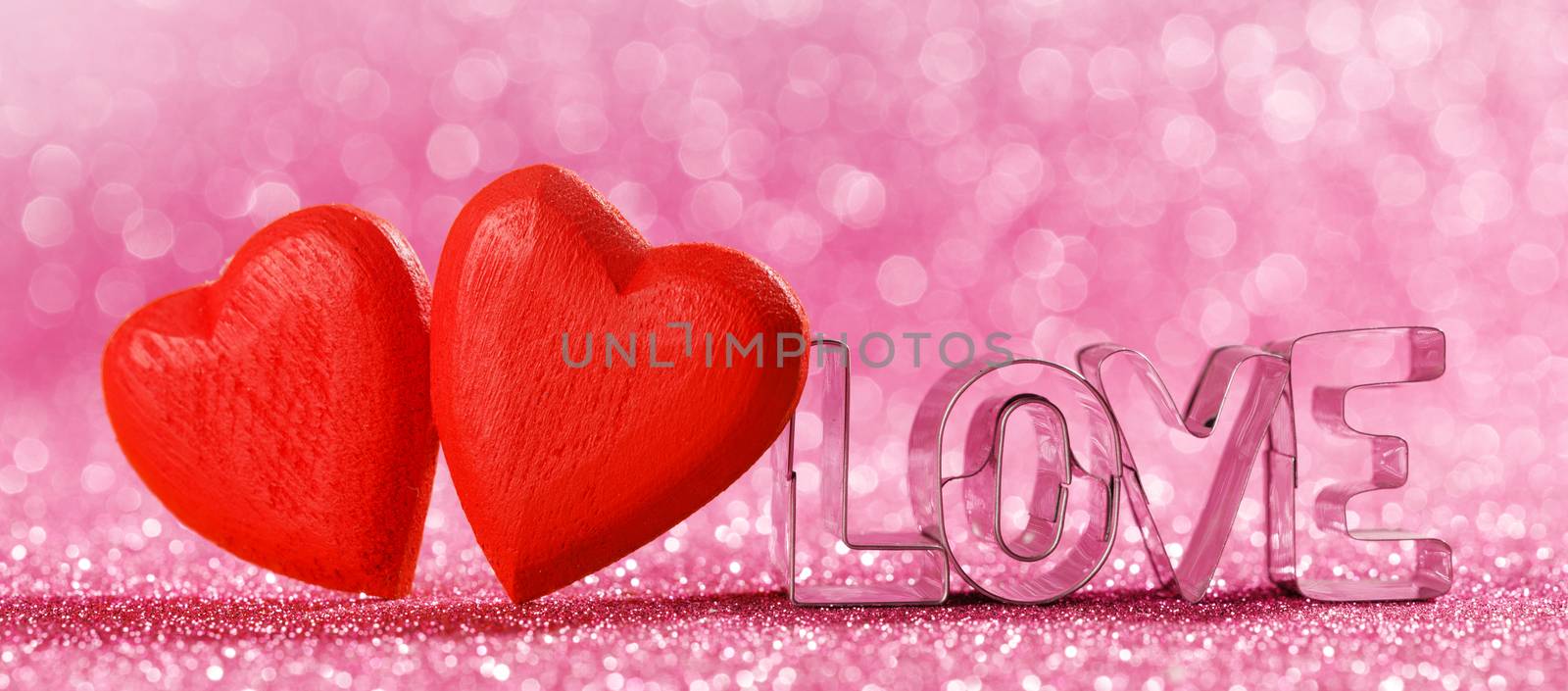 Two red handmade wooden hearts and word love on pink bright glitter lights bokeh background