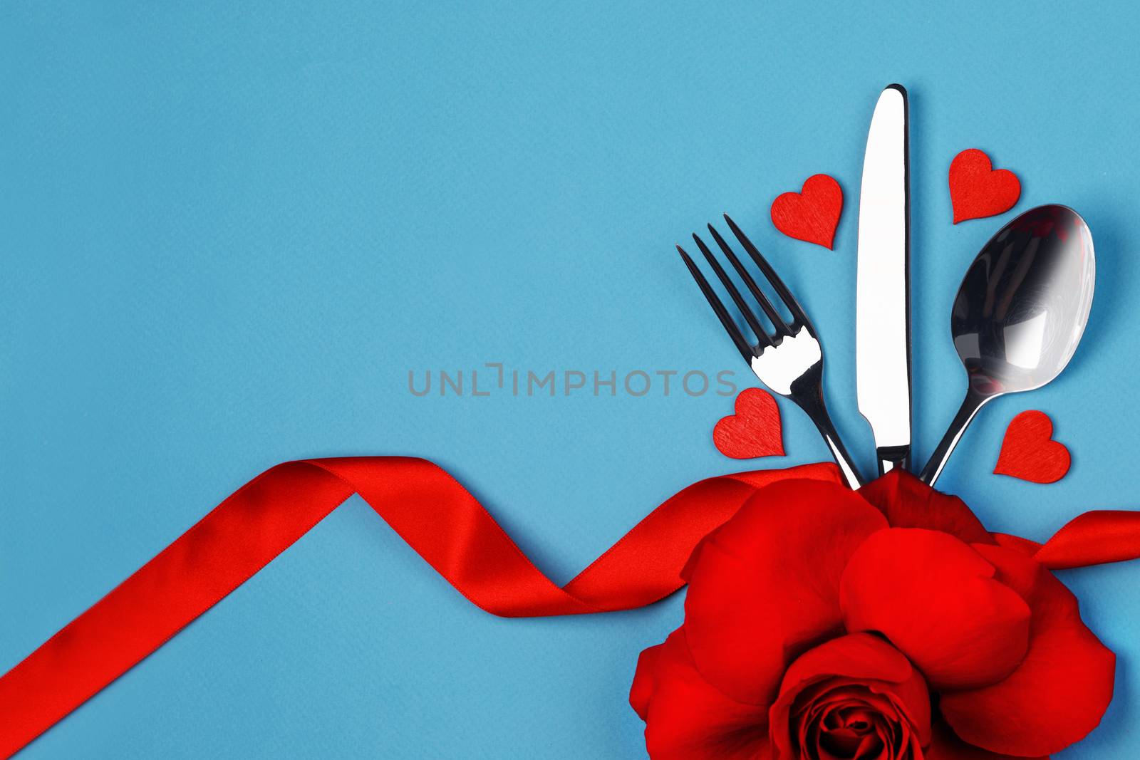Cutlery set tied with silk ribbon rose flower and hearts on blue background Valentine day dinner concept