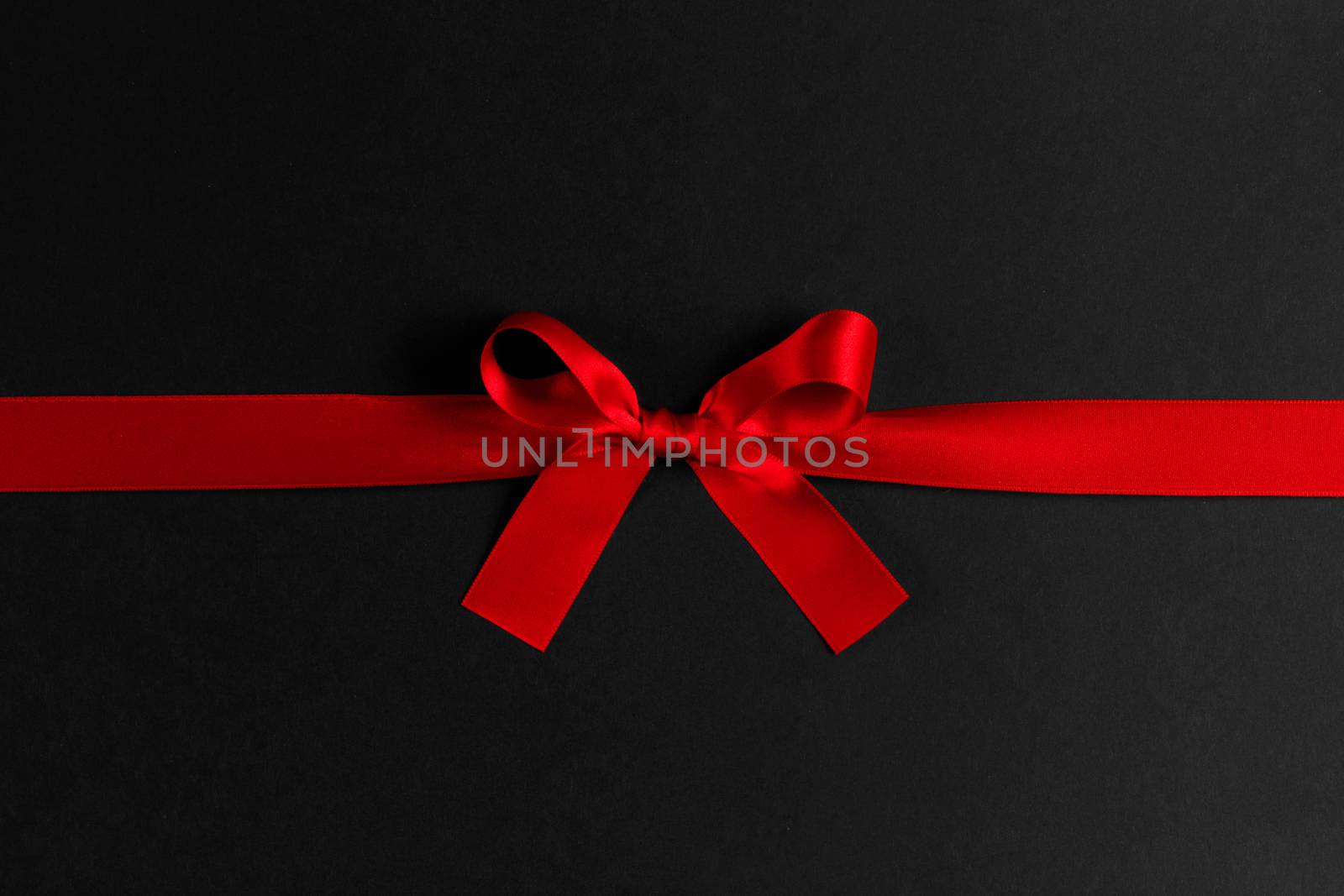 Shiny red satin ribbon and bow on black background. Holiday gift concept